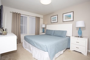 Une chambre à coucher avec un grand lit, deux tables de chevet, un bureau et une fenêtre avec des rideaux.