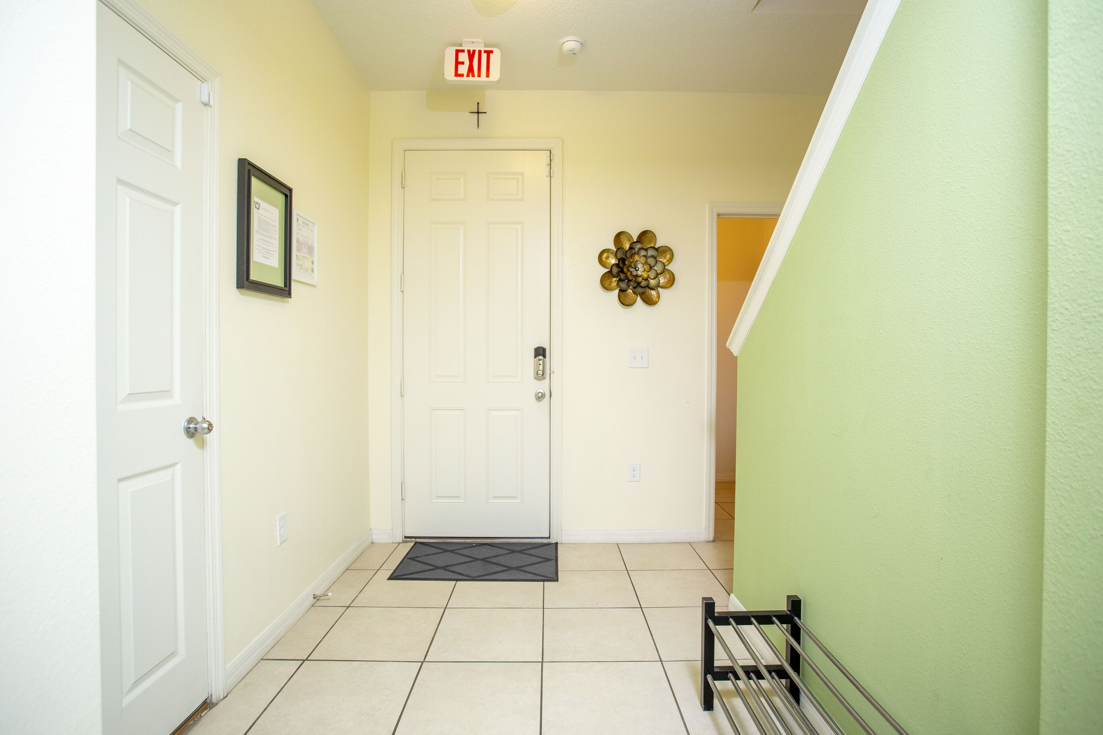 A hallway with a white door, a black metal bench, and a wall-mounted exit sign.