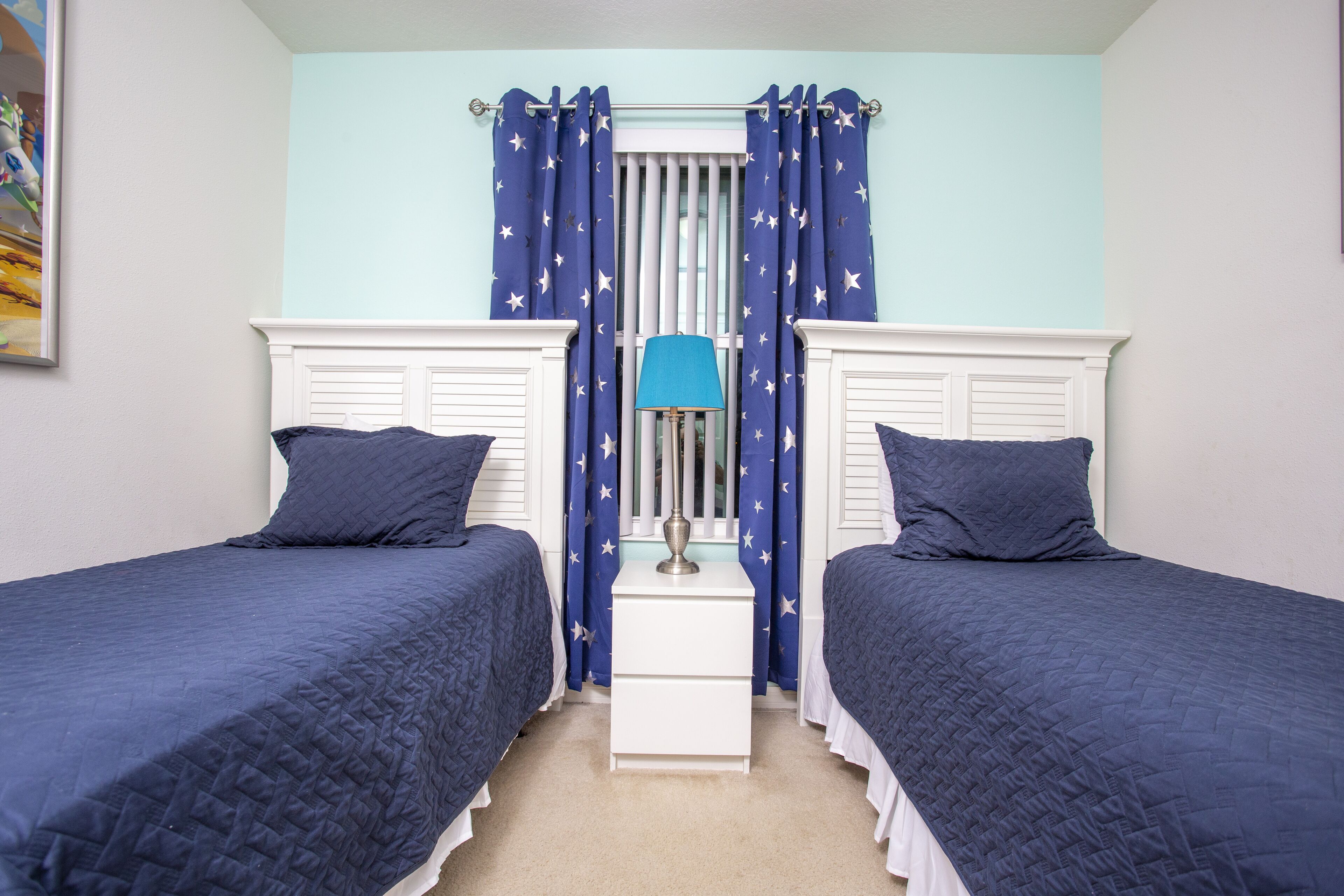 A bedroom with two beds, a nightstand, a lamp, and star-patterned curtains.
