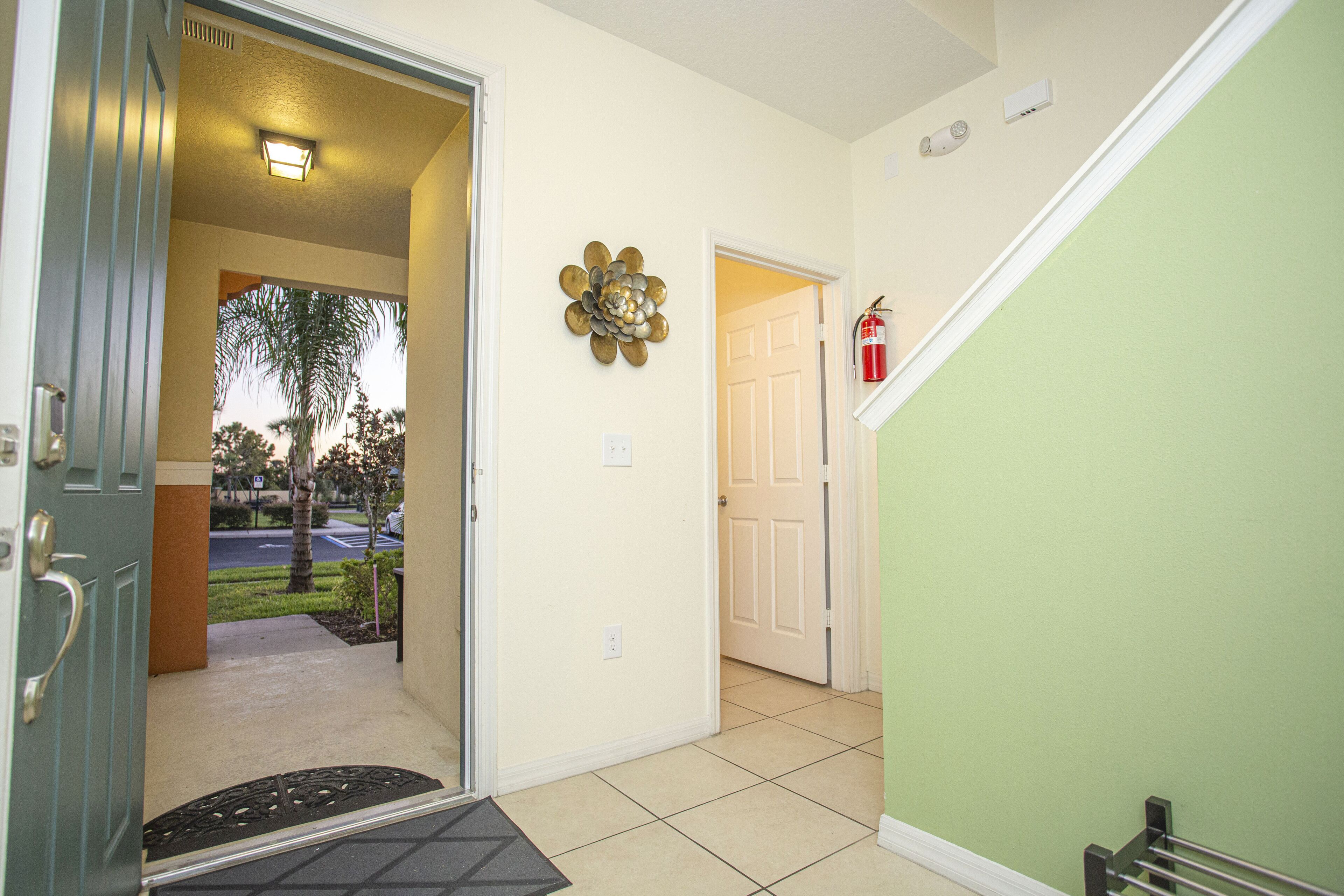 A hallway with a door leading to a parking area, a fire extinguisher on the wall, and a doormat at the entrance.