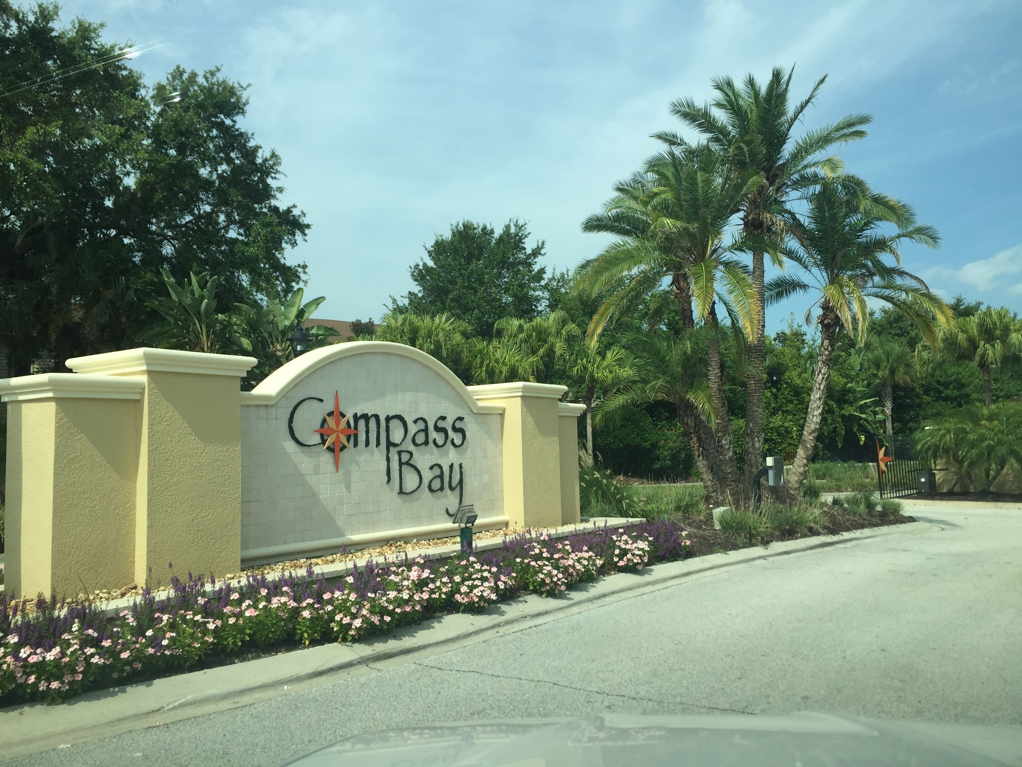 A sign with "Compass Bay" written on it, surrounded by palm trees and flowers.