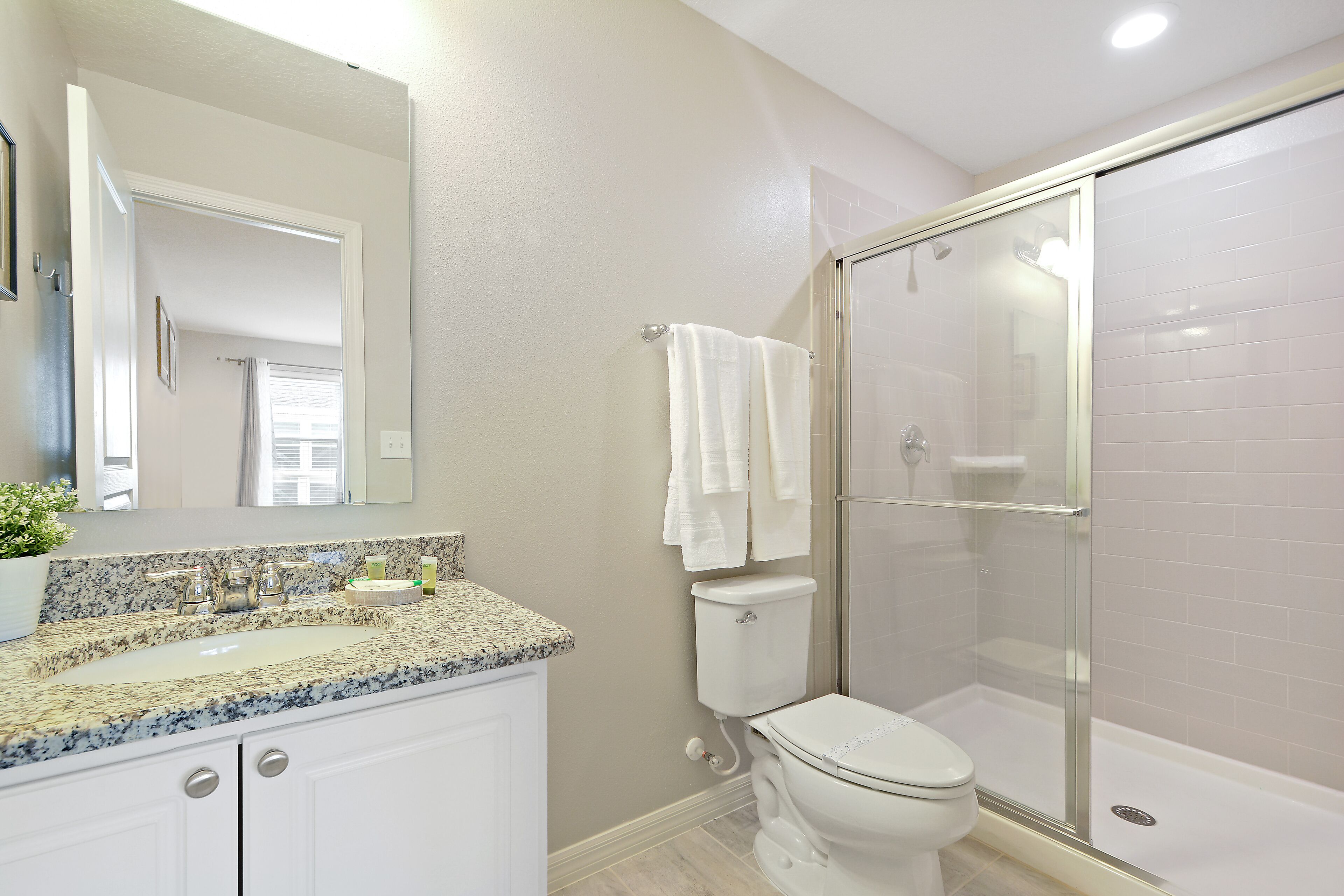 Een badkamer met een wastafel met granieten blad, een toilet en een douche met glazen wanden.