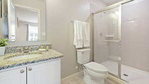 A bathroom with a granite countertop sink, a toilet, and a glass-enclosed shower. - Family Friendly 4 Bedroom close to Disney in Compass Bay Resort 5108 (Kissimmee)