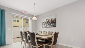 Un espace repas avec une table et des chaises, un panneau de sortie, un tableau et une vue à travers une porte vitrée.