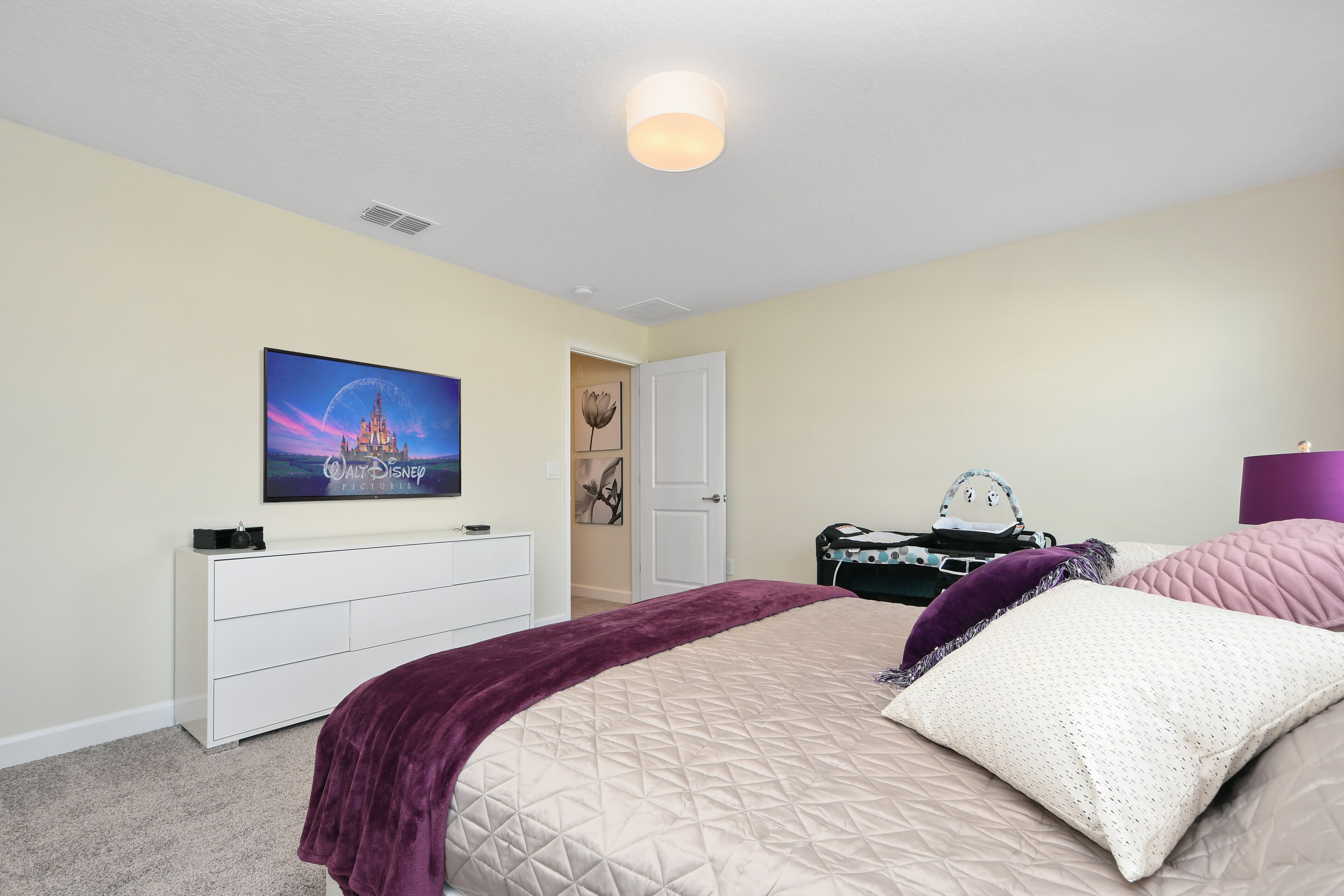 A bedroom with a bed, a dresser, a television, and a door leading to another room.