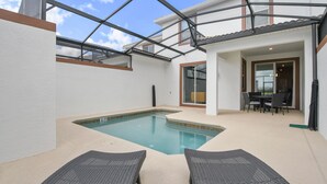 A swimming pool with two lounge chairs, a covered patio, and a dining area with a table and chairs.