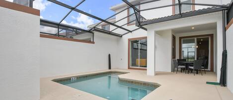 Une piscine avec deux chaises longues, un patio couvert et un coin repas comprenant une table et des chaises.