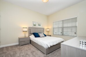 A bedroom with a bed, bedside tables, lamps, a nightstand, a dresser, and a window with blinds. - Charming 4Bd w/ Pool @ Storey Lake Resort Orlando 4861 (Kissimmee)