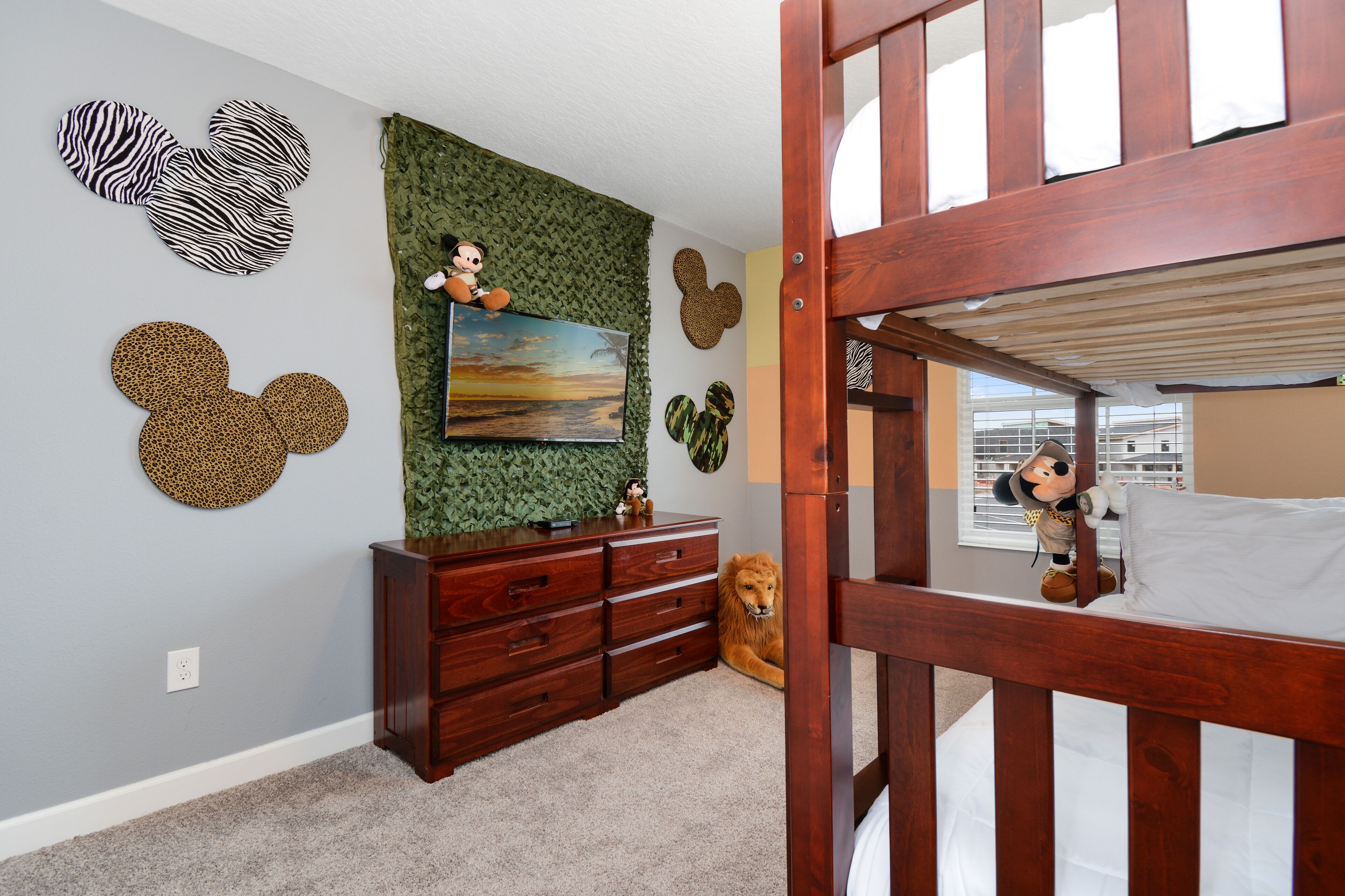 A child's room with a bunk bed, a dresser, and wall decorations including Mickey Mouse ears and a painting.