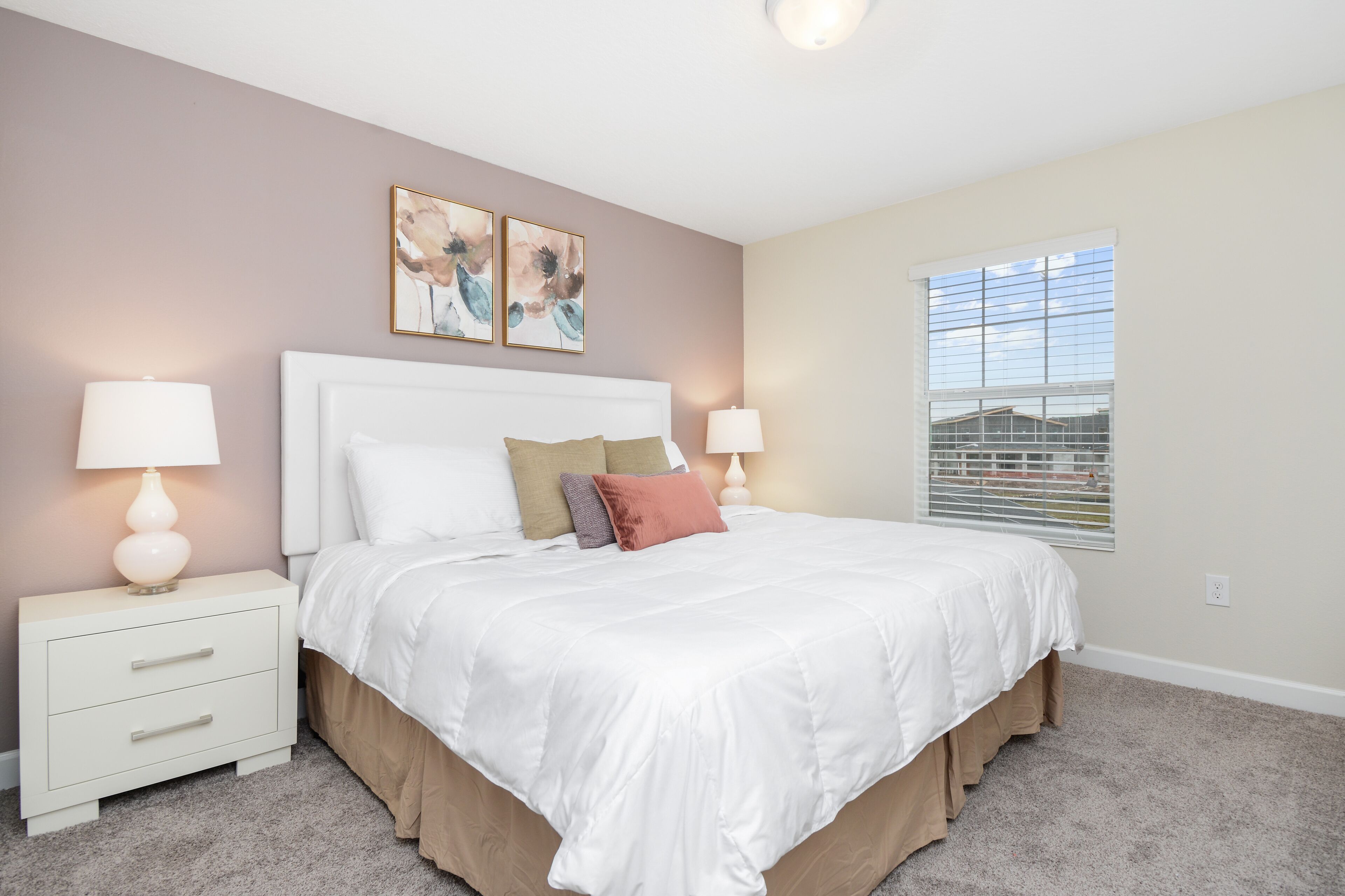 A bedroom with a large bed, two bedside tables, and a window with blinds.