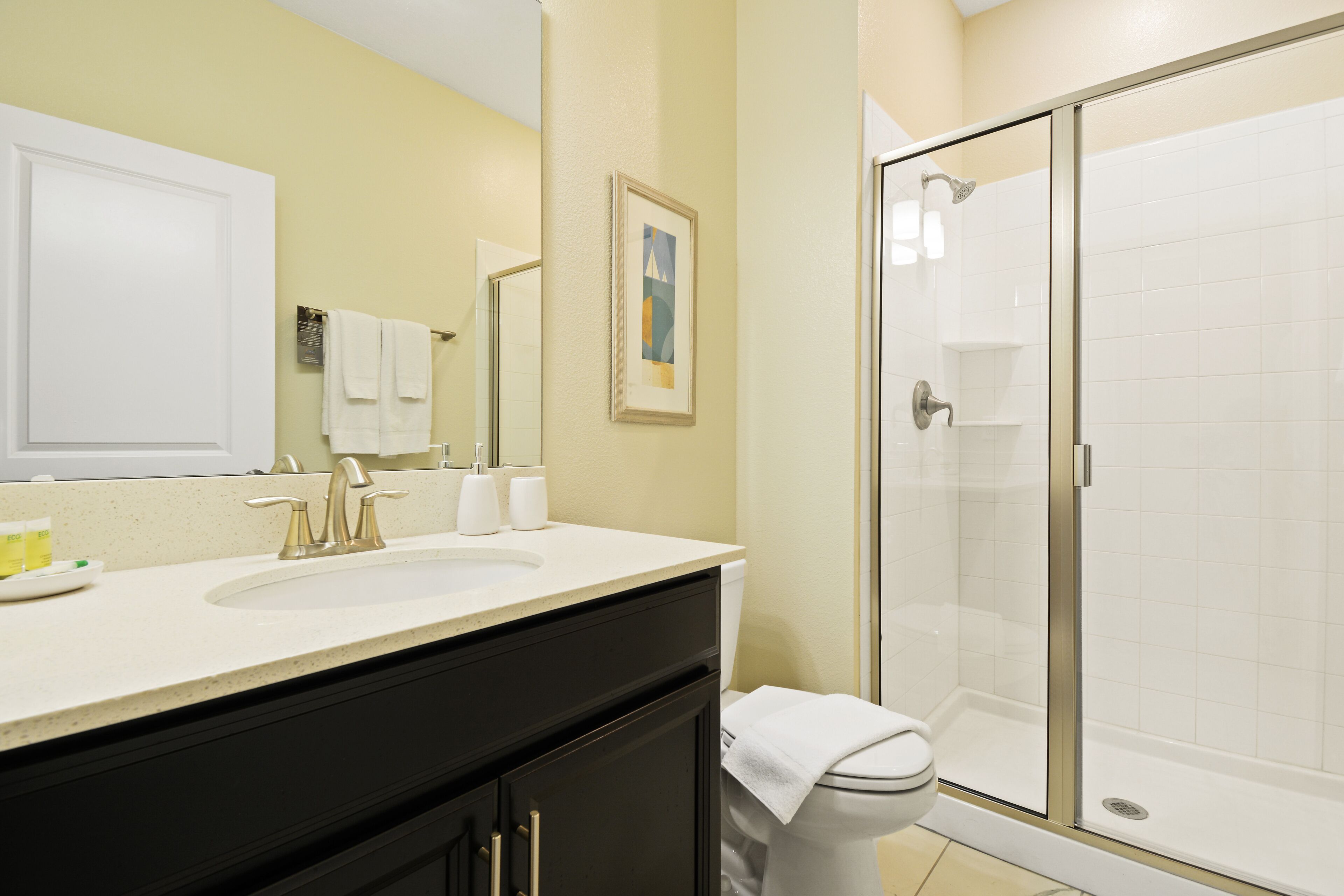 A bathroom with a sink, mirror, towel rack, and a glass-enclosed shower.