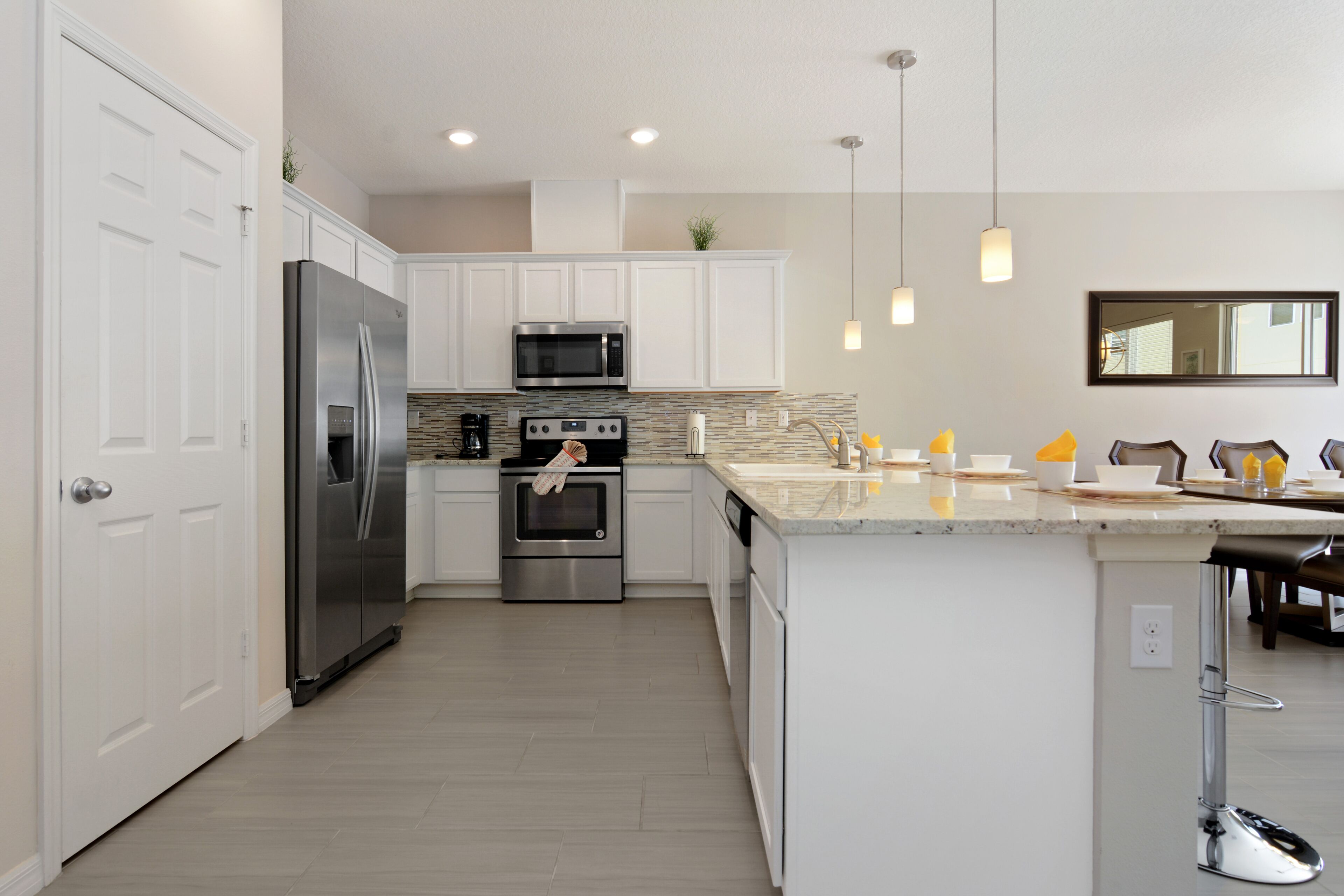 A modern kitchen with white cabinets, stainless steel appliances, a granite countertop, and pendant lighting.