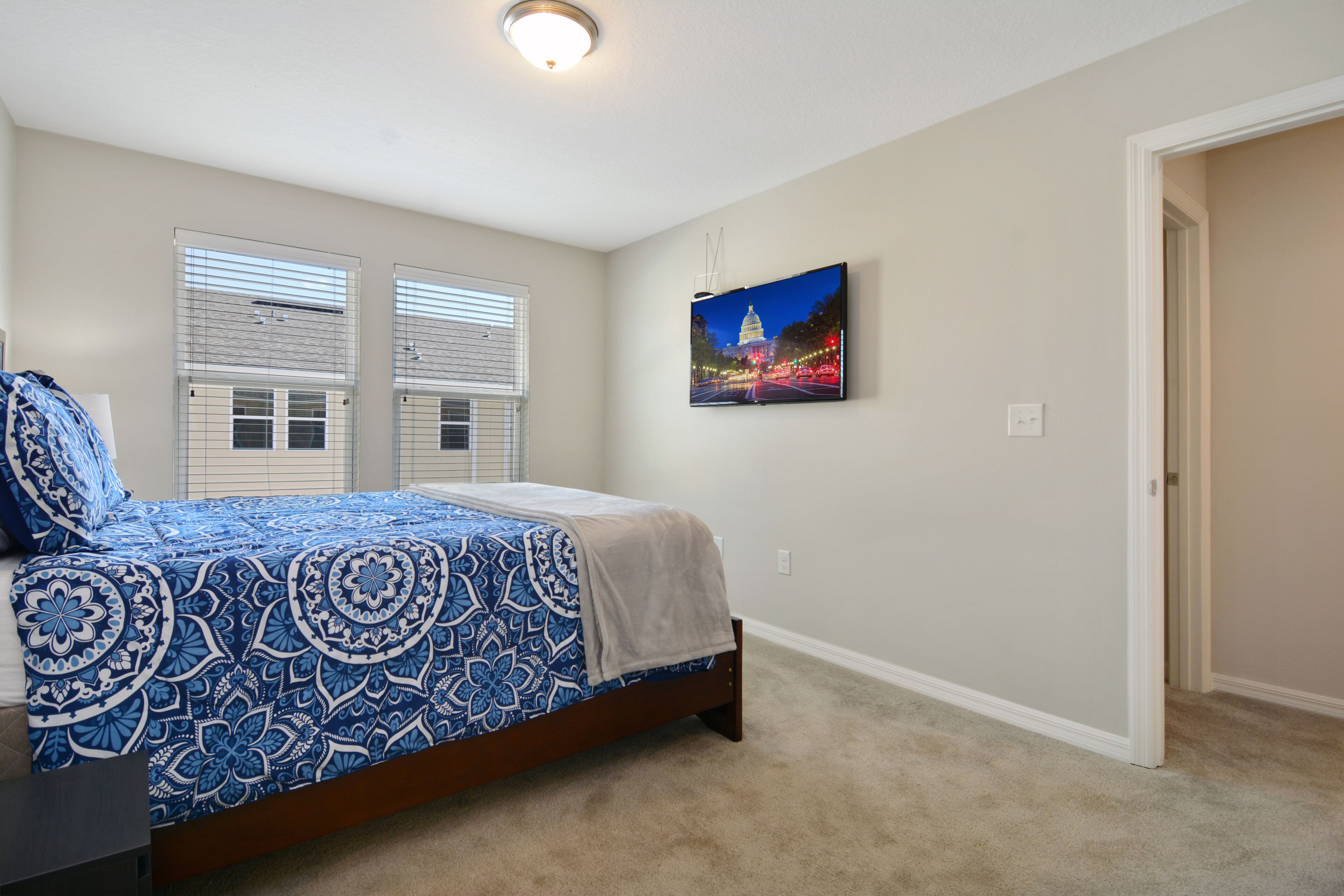 A bedroom with a bed, two windows with blinds, a wall-mounted picture, and a carpeted floor.