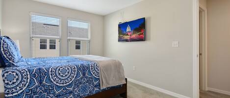 A bedroom with a bed, two windows with blinds, a wall-mounted picture, and a carpeted floor.