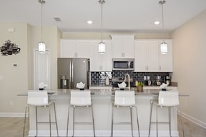 A modern kitchen with white bar stools, stainless steel appliances, and pendant lighting. - Family Friendly 4Bd PV Pool @ Storey L Resort 4896 (Kissimmee)