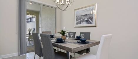 A dining area with a wooden table, grey and white chairs, a modern chandelier, and a framed picture on the wall.