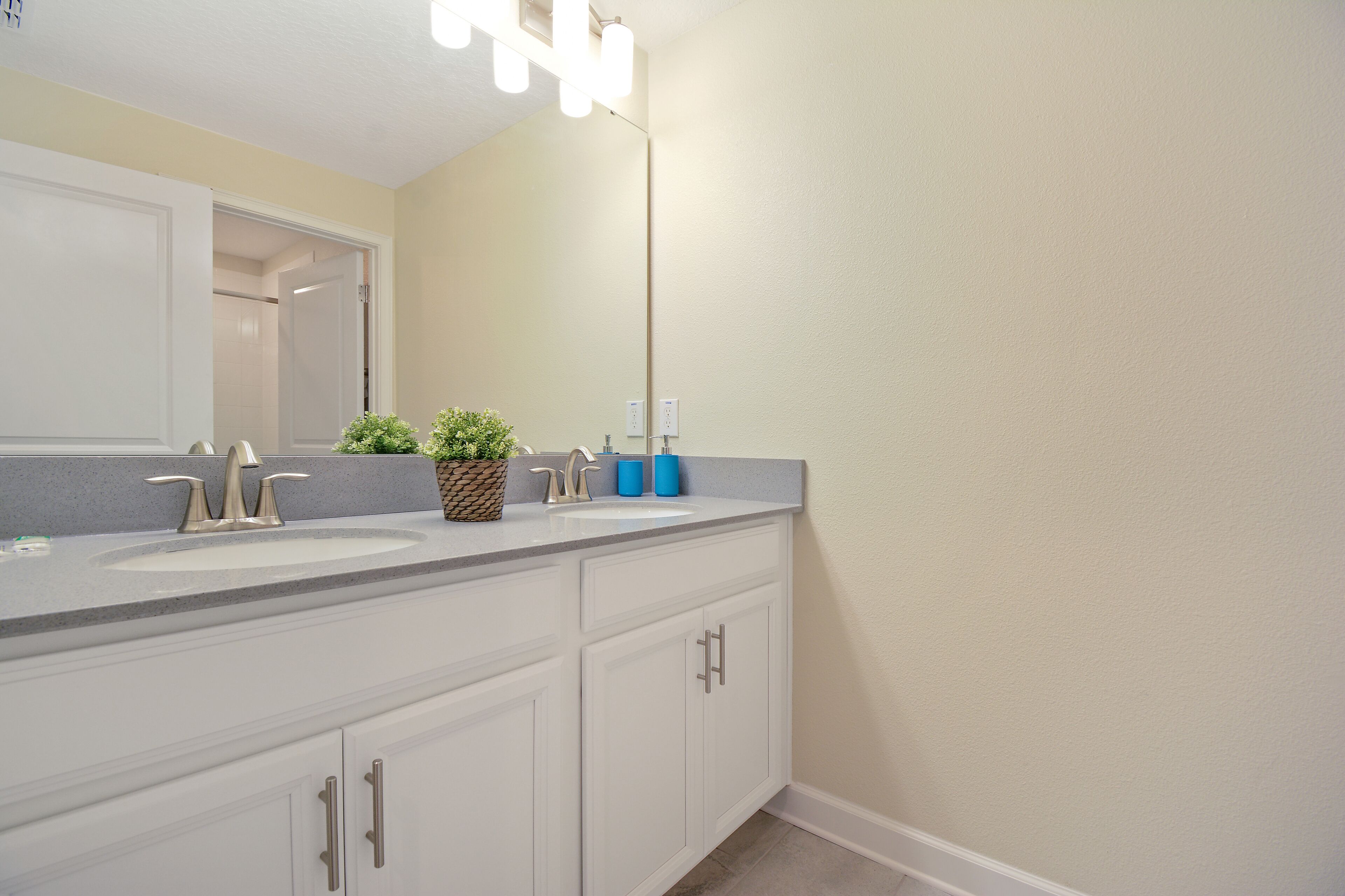 A bathroom with a double sink, white cabinets, and a mirror.