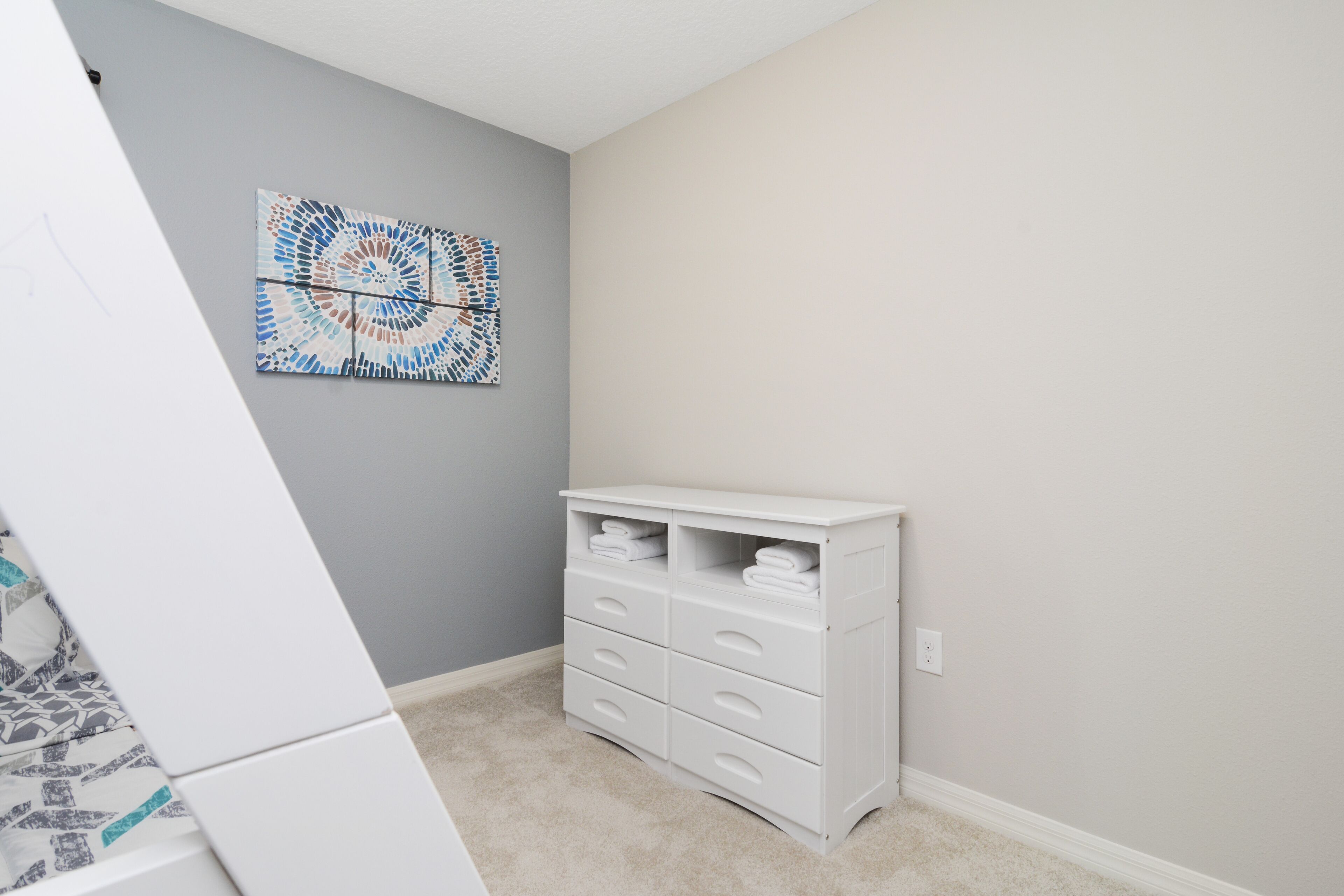 A room with a white dresser, a gray wall, and a blue and white abstract painting.