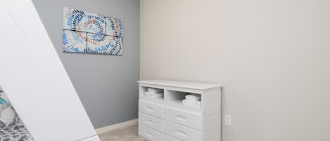 A room with a white dresser, a gray wall, and a blue and white abstract painting.