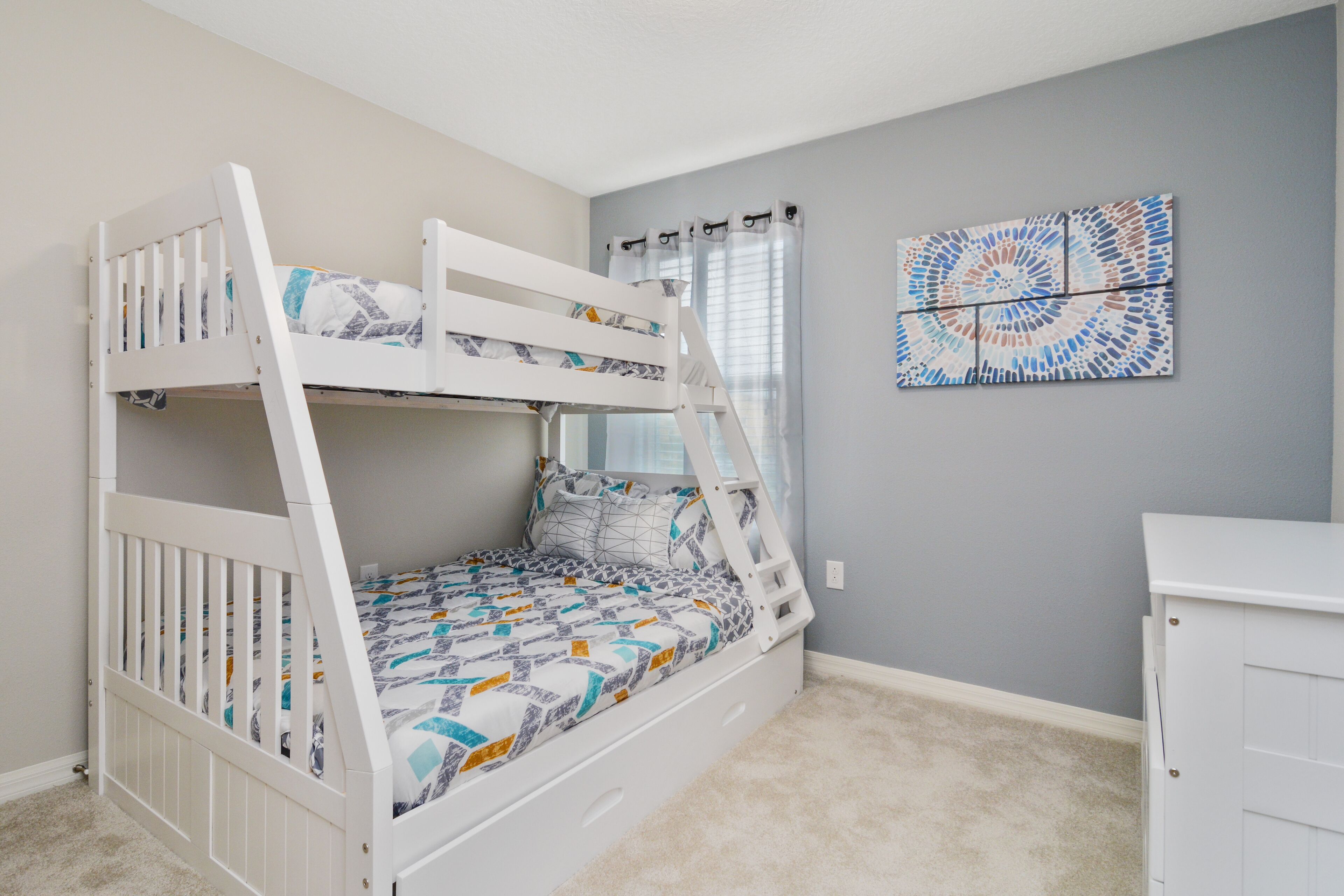Uma cama de beliche com escada, uma escrivaninha e uma parede com padrão de mosaico circular.