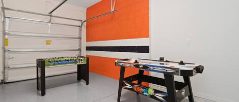A room with two foosball tables, one with a colorful tablecloth and another with a black frame.