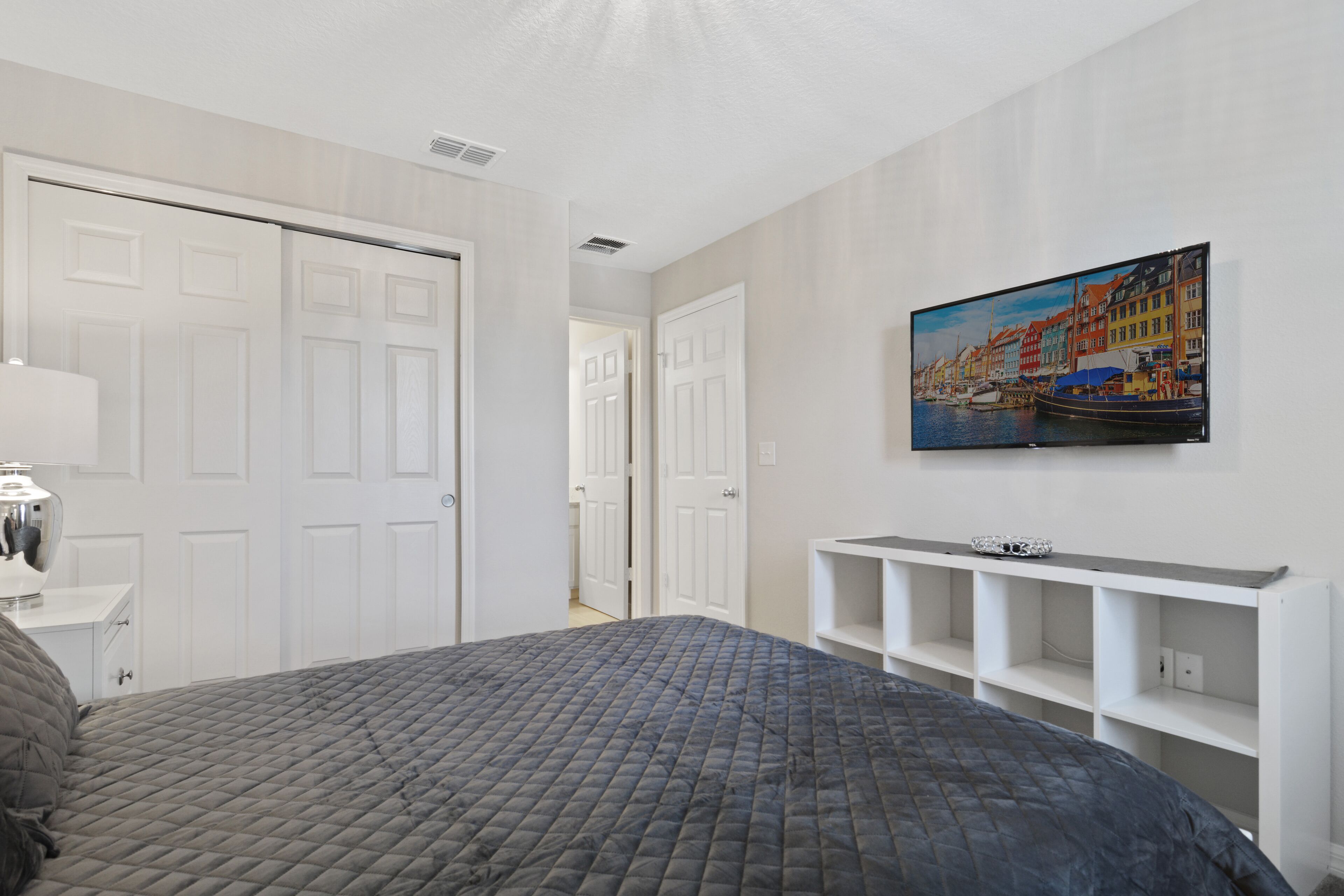 Ein Schlafzimmer mit einem Bett, einem an der Wand befestigten Fernseher und einer weißen Tür.