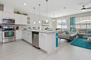 Une cuisine moderne avec des armoires blanches, des appareils en acier inoxydable et un mur d’accent de couleur turquoise.