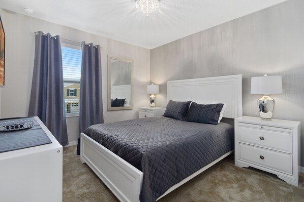 Une chambre à coucher comprenant un lit, des tables de chevet, une commode, un miroir et un lustre.
