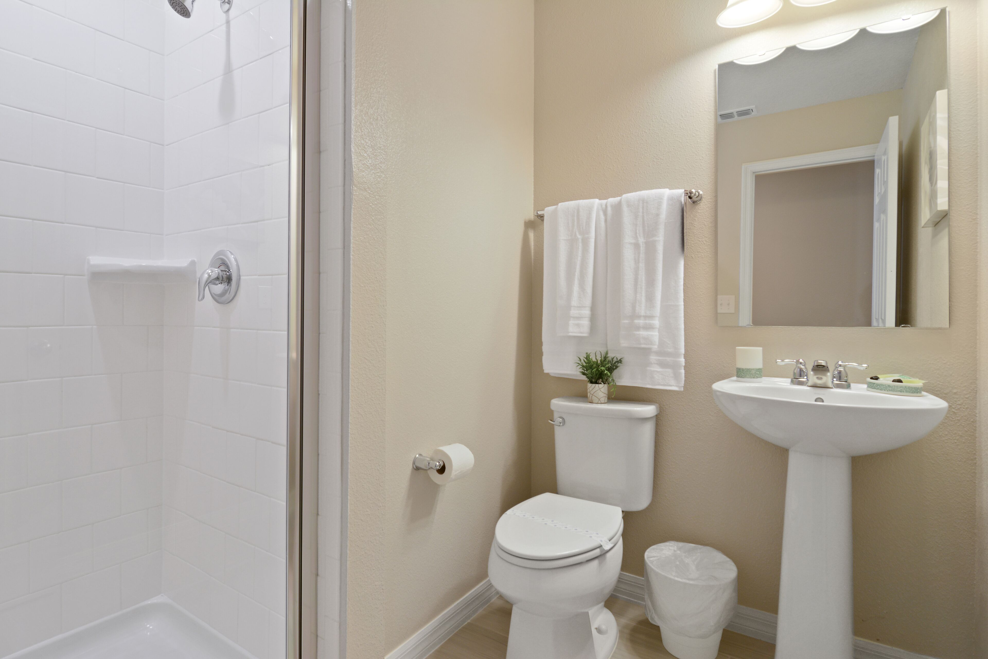 A bathroom with a shower, toilet, sink, and a mirror.