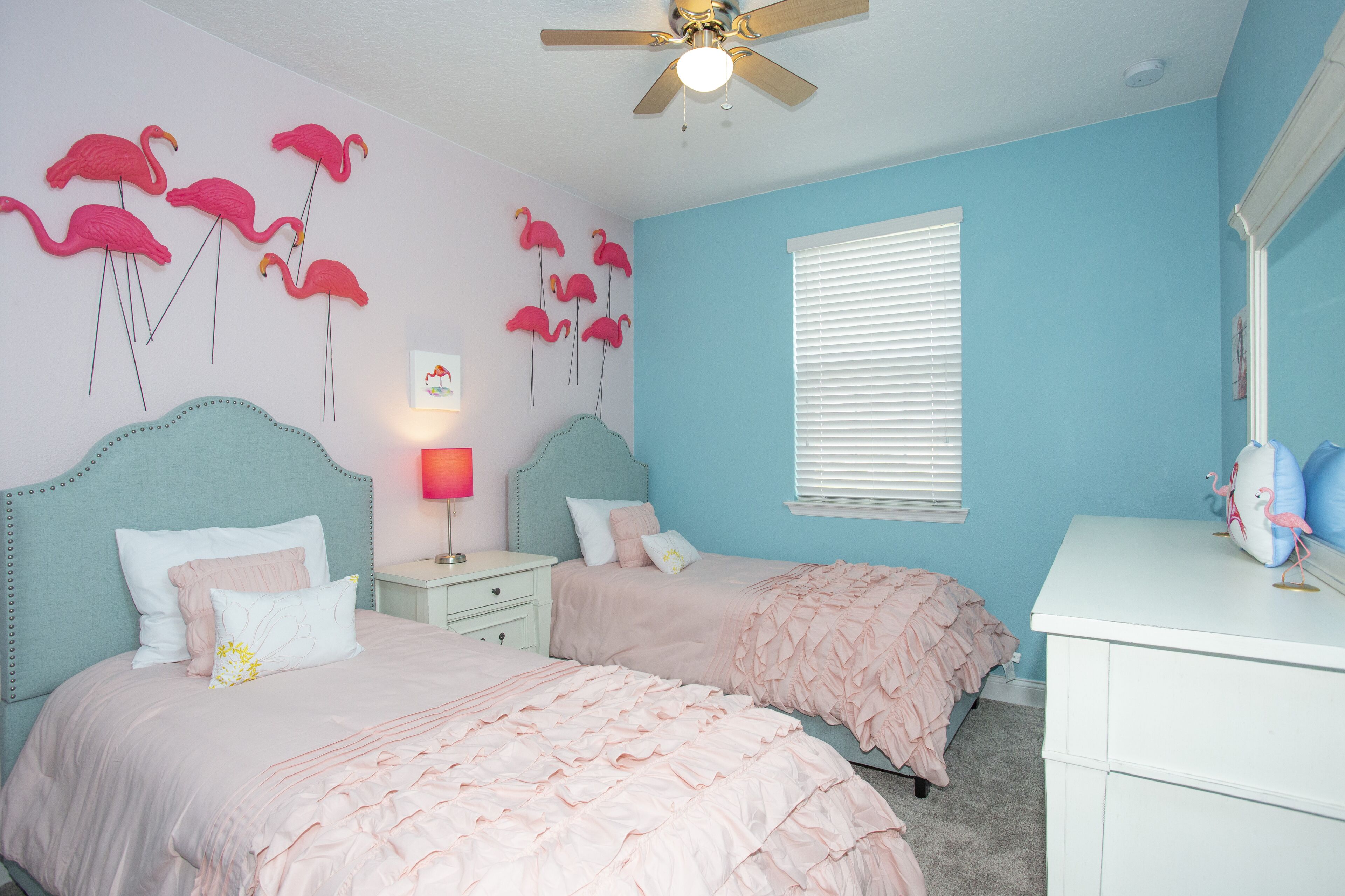 Quarto com duas camas, ventoinha no teto, janela com persianas e decoração nas paredes.