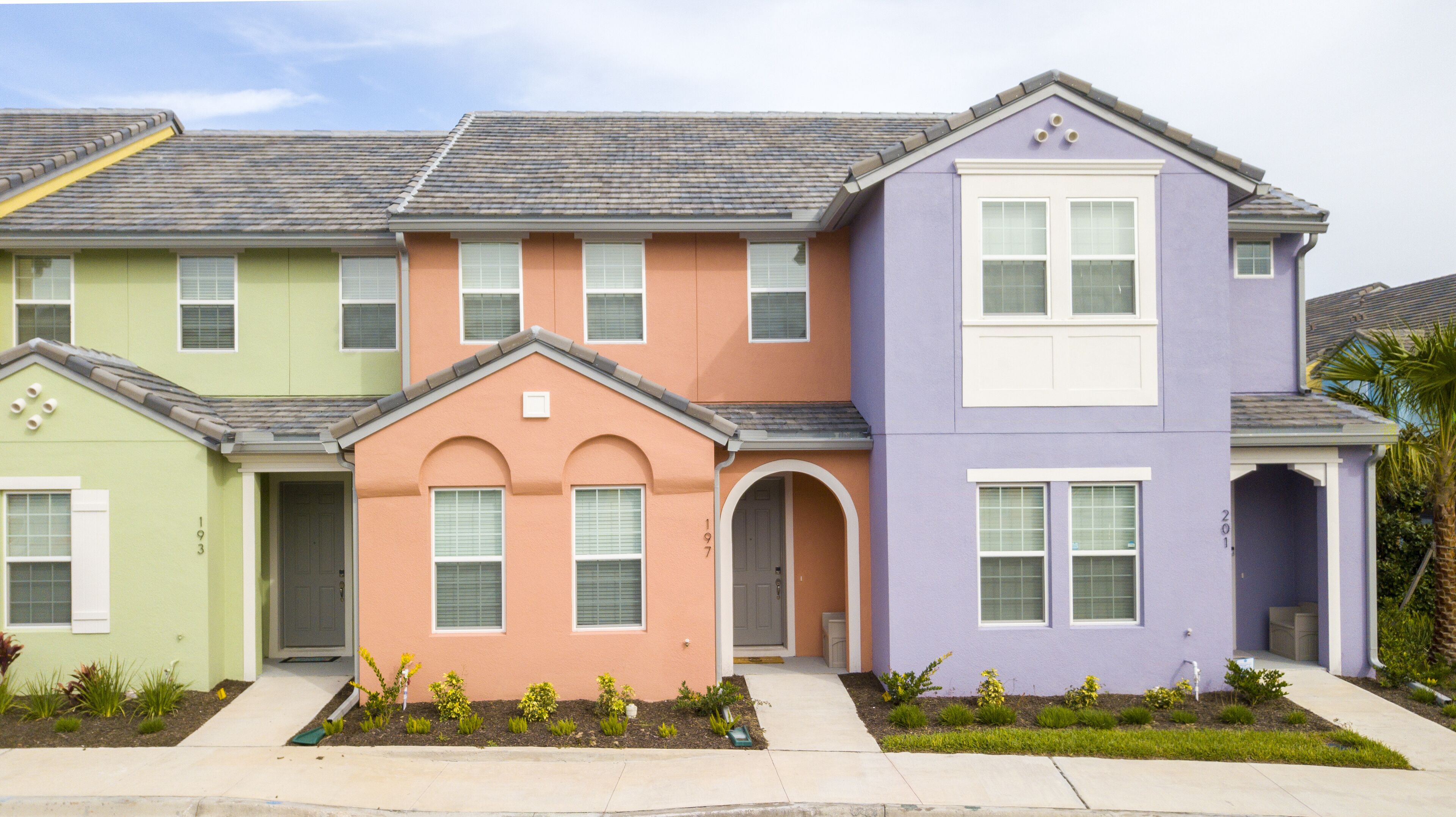 A row of three-story houses with distinct pastel colors, each featuring a front door, windows, and a small garden area.