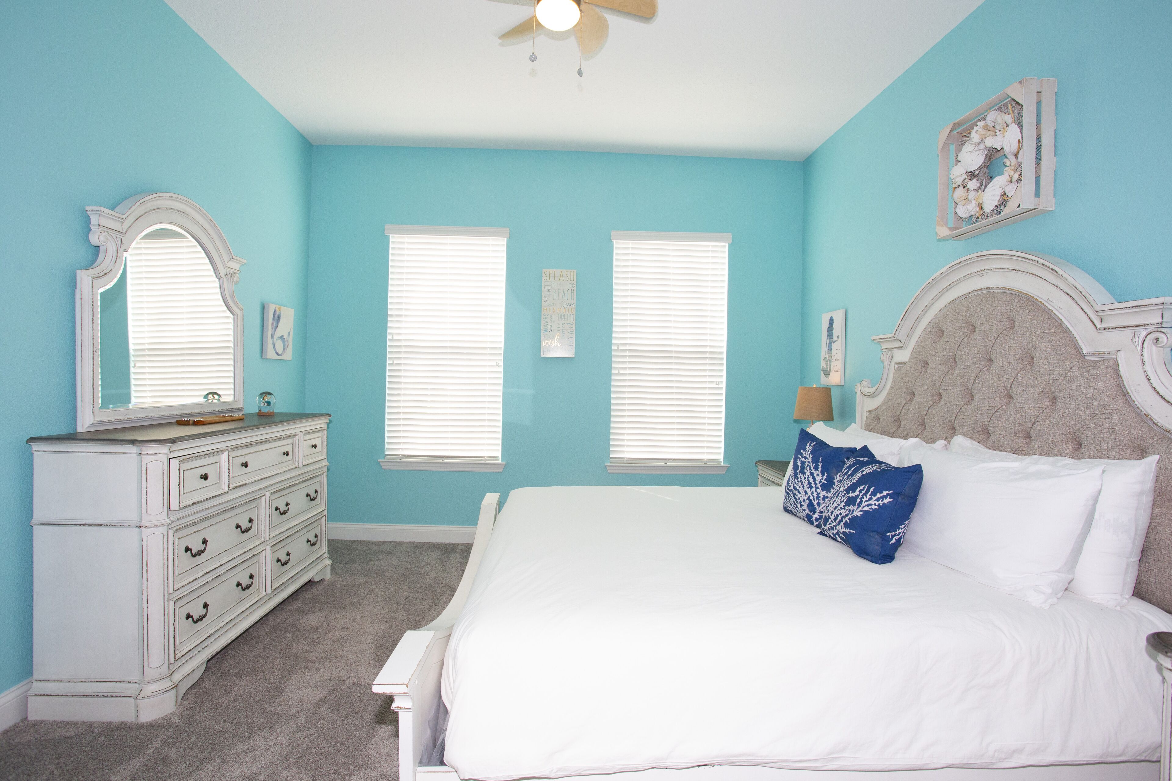 A bedroom with a bed, dresser, and two windows with blinds.