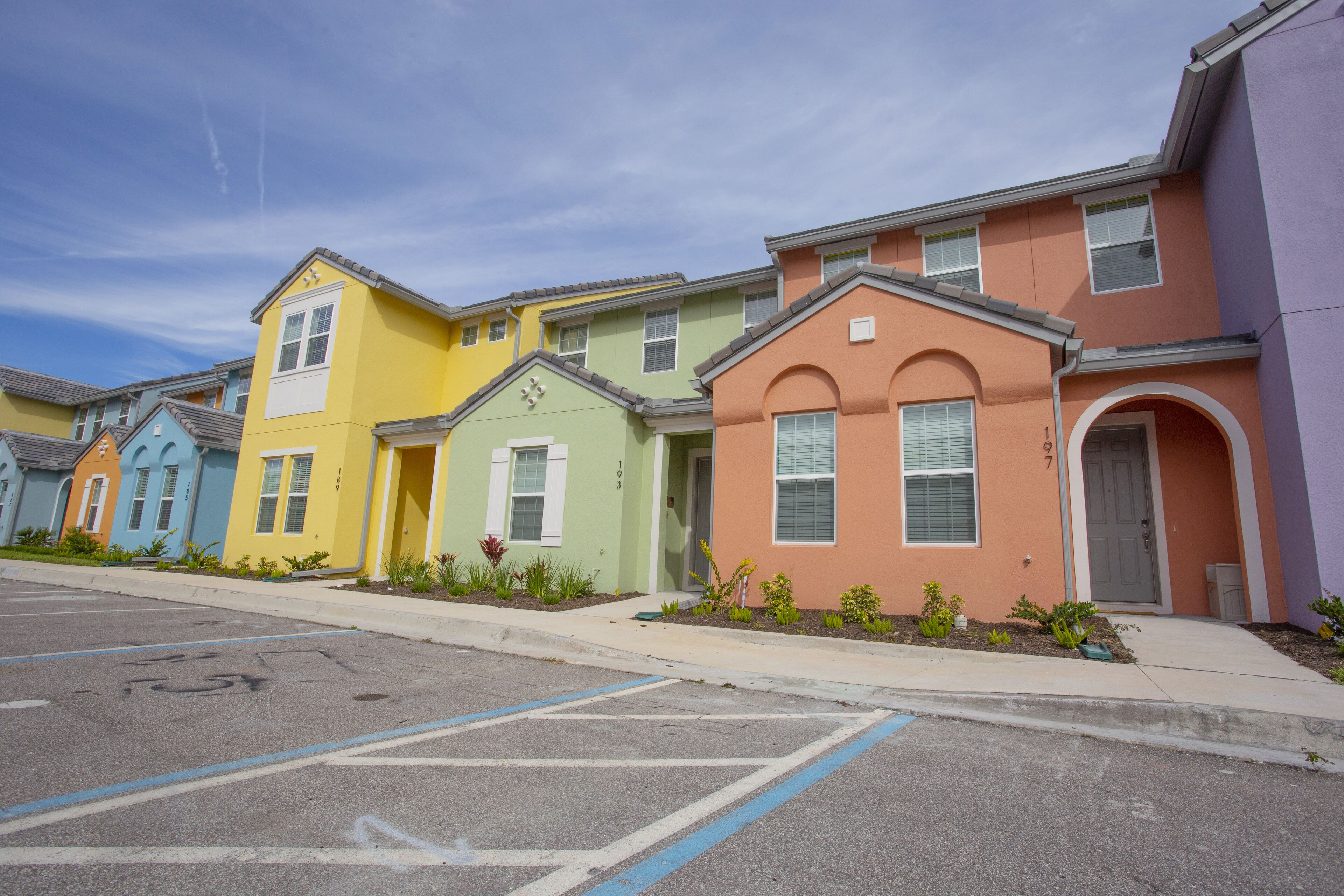 A row of colorful townhouses with a parking lot in front.