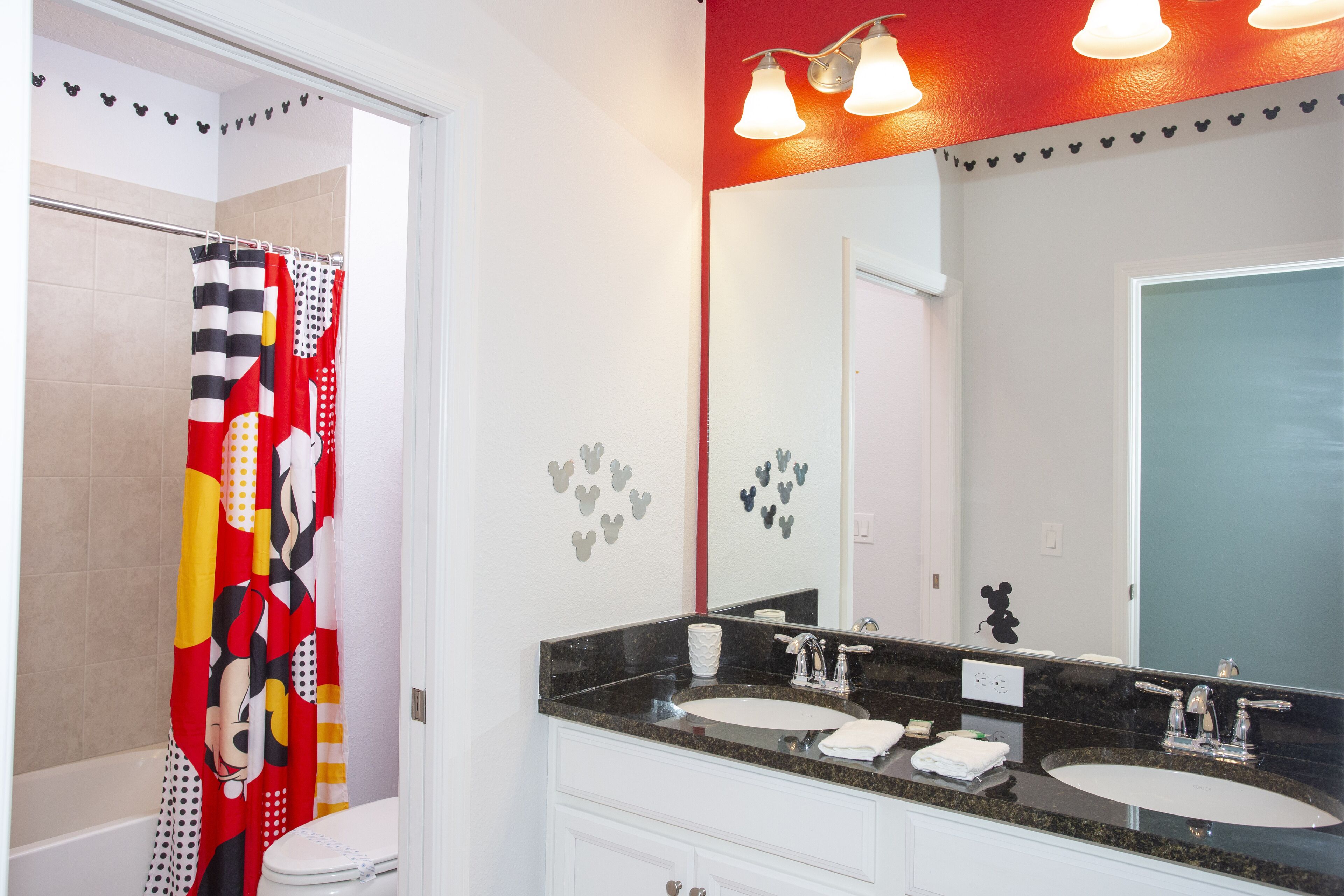 A bathroom with a Mickey Mouse shower curtain, a double sink vanity, and a large mirror.
