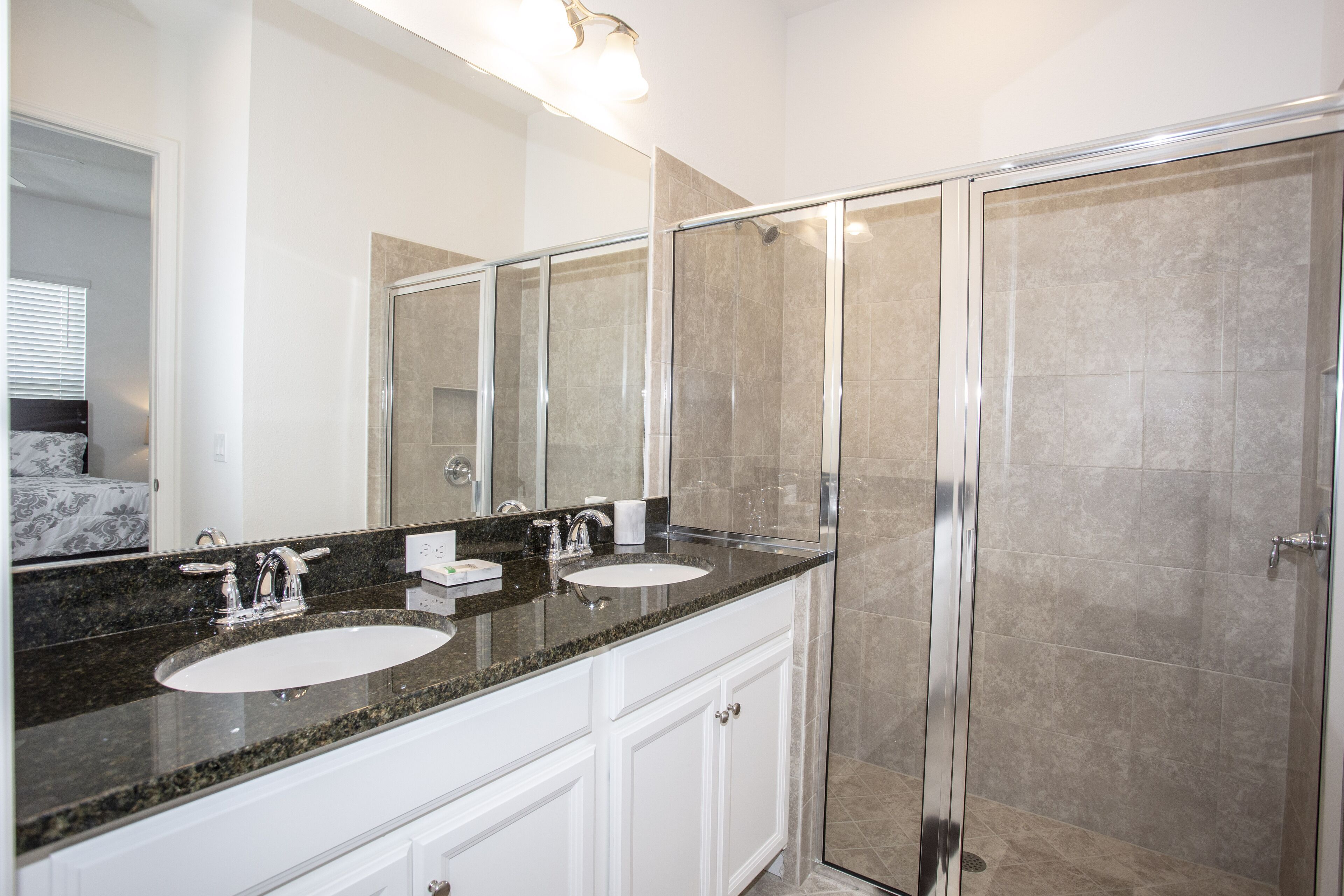 Une salle de bain moderne avec deux lavabos, un grand miroir et une douche à parois de verre.