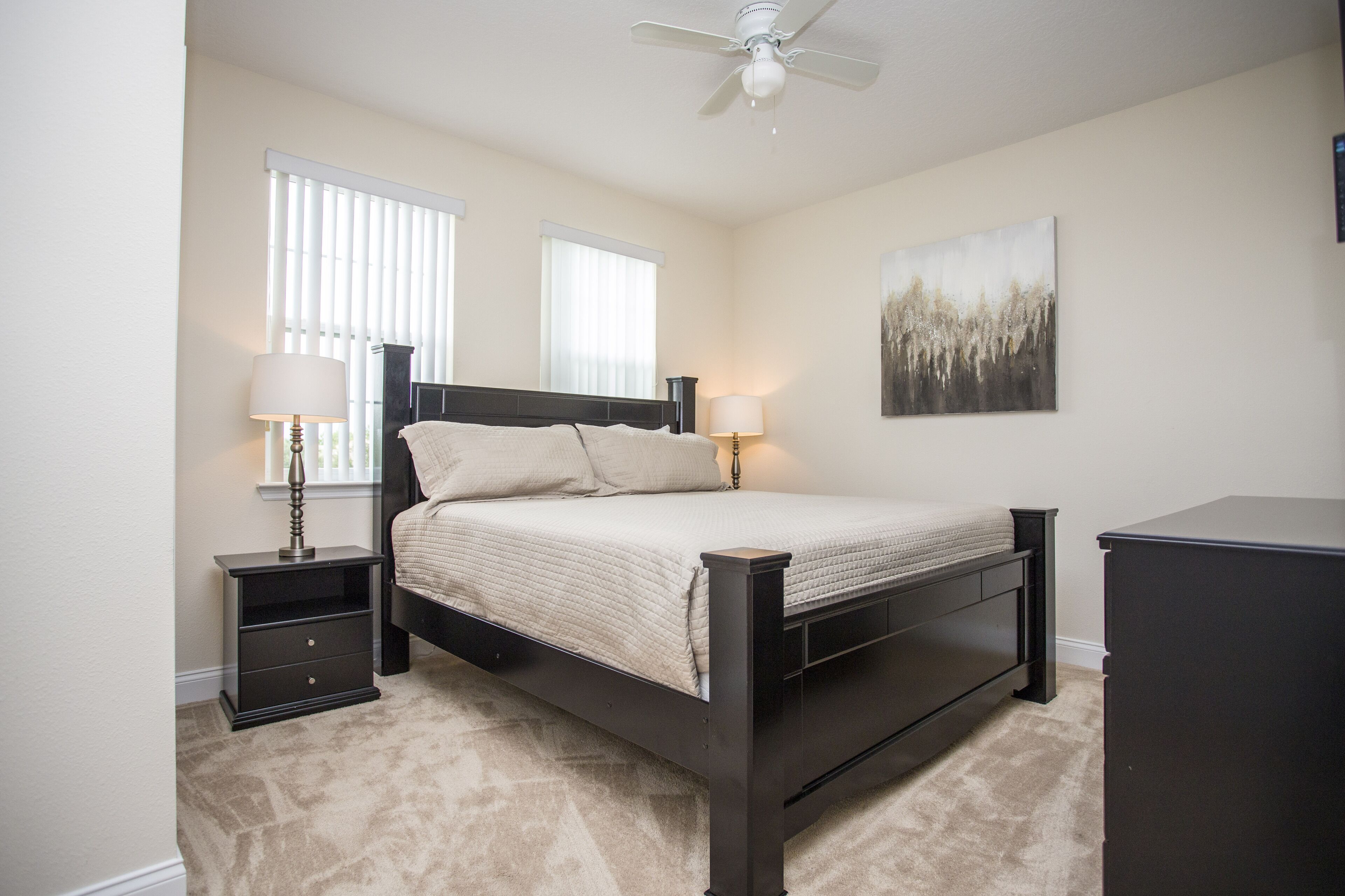 A bedroom with a bed, nightstands, a ceiling fan, and a painting on the wall.