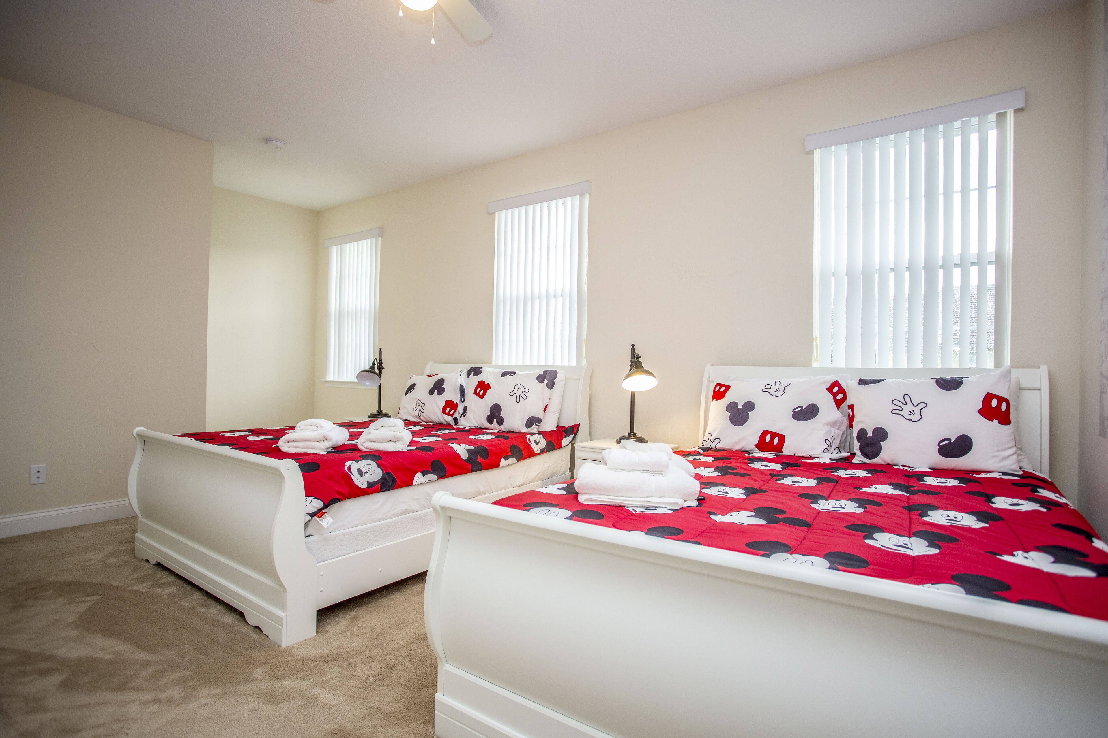 A hotel room with two beds, each with a Mickey Mouse themed bedspread and pillows.