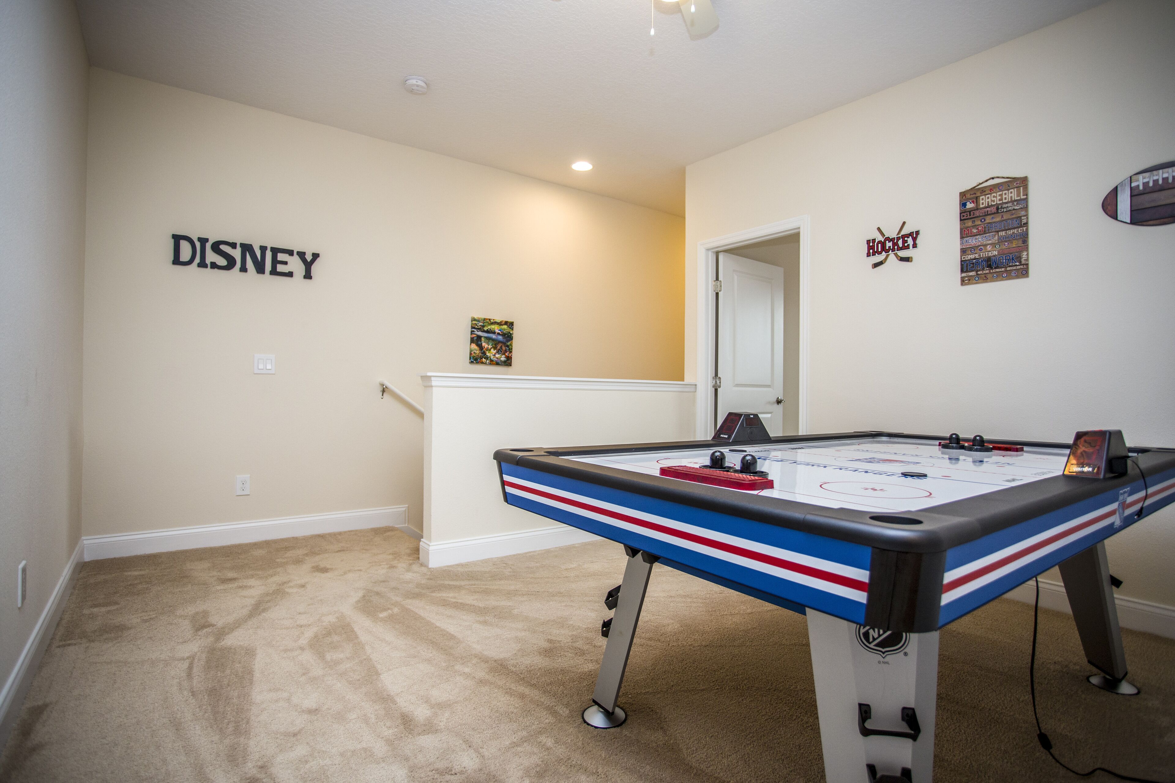 A room with a pool table, a wall with the word "DISNEY" and a hockey sign, and a door leading to another room.