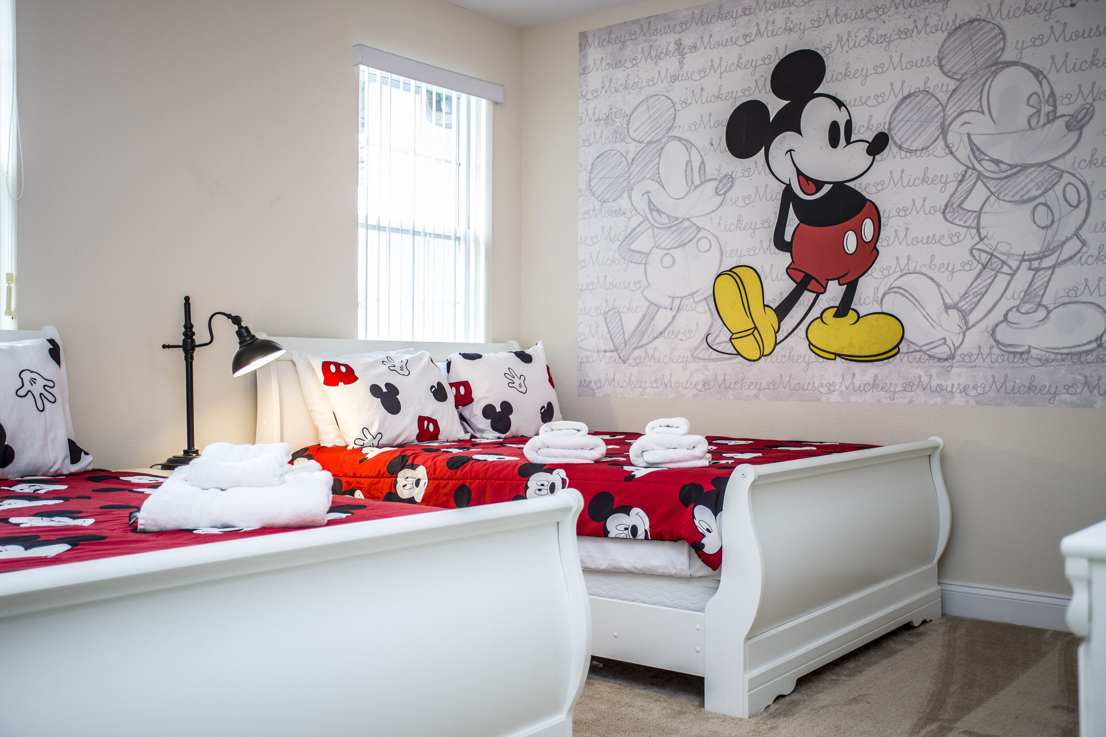 Une chambre avec une couvre-lit aux motifs de Mickey Mouse, une lampe et une fresque murale représentant Mickey Mouse.