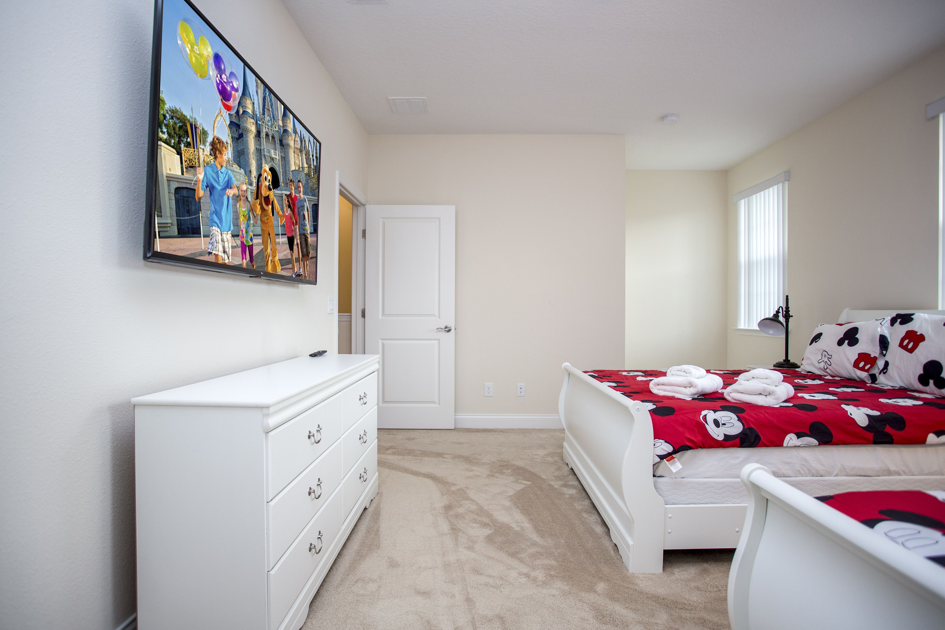 A bedroom with a bed, a dresser, a nightstand, and a wall-mounted TV.