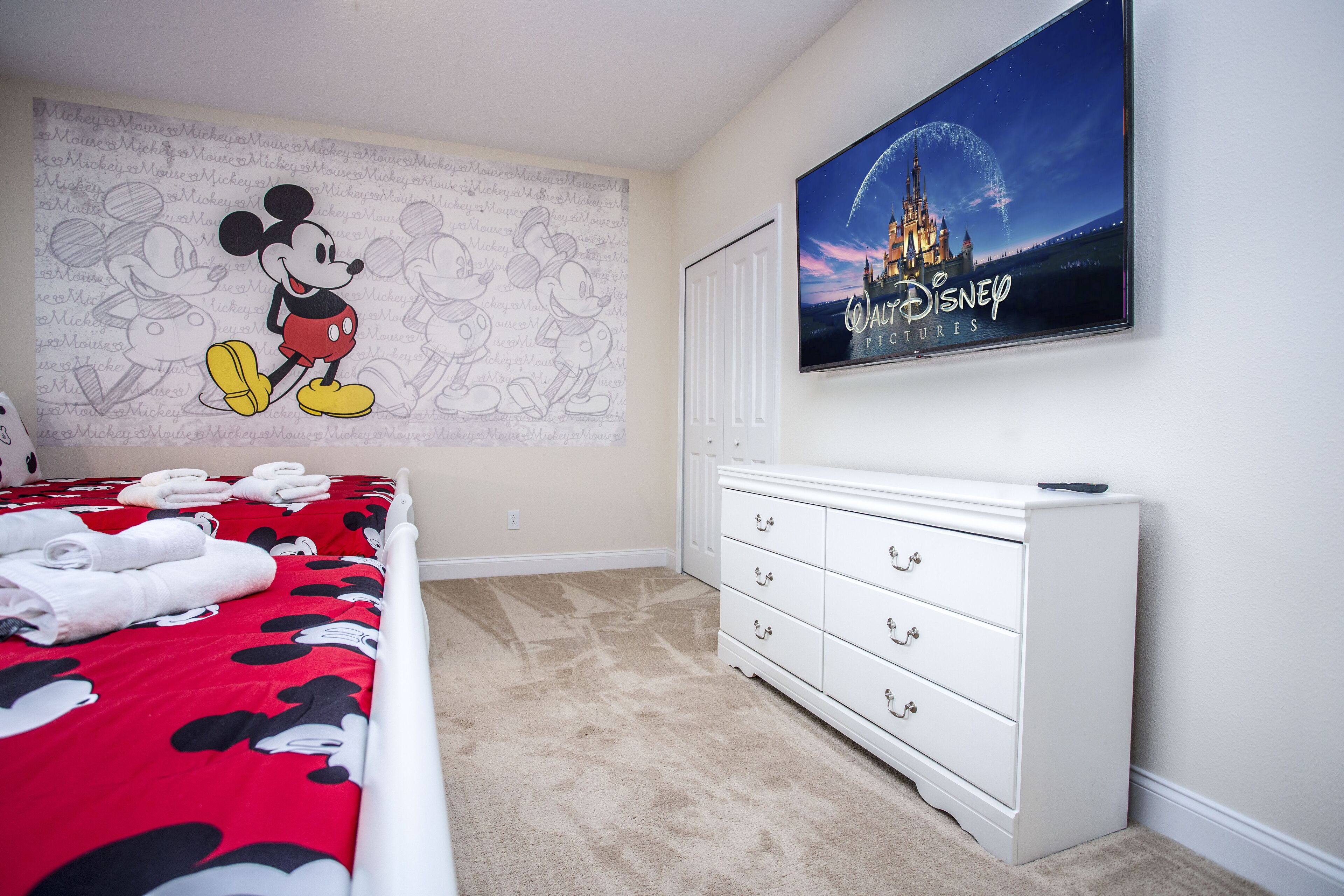 A hotel room with a Mickey Mouse themed bedspread, a large Disney movie poster, and a white dresser.