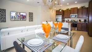 Un espace repas moderne avec une table en verre, des chaises blanches et des serviettes orange.