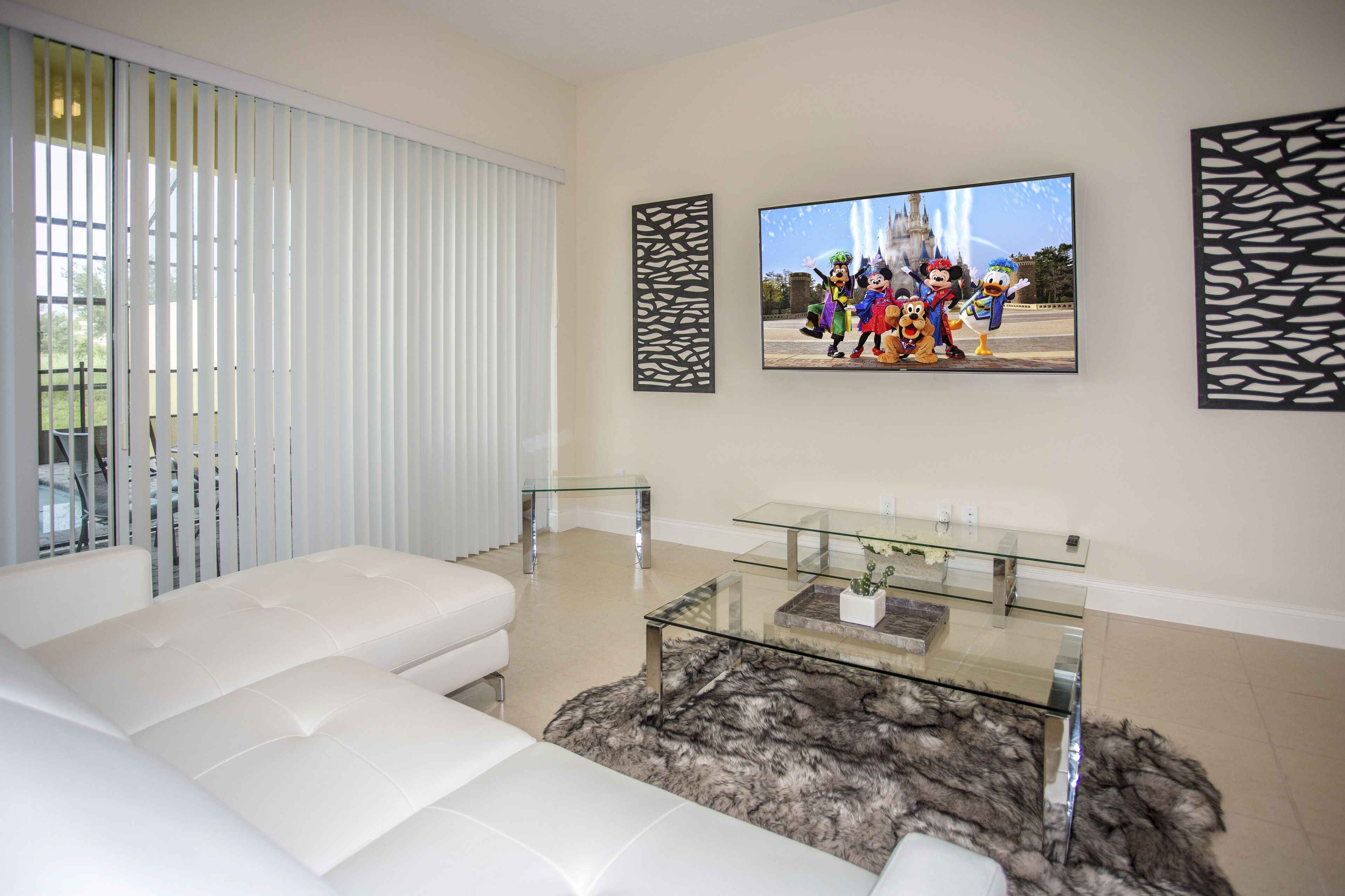 A modern living room with a white sofa, a glass coffee table, and a large flat-screen TV mounted on the wall.