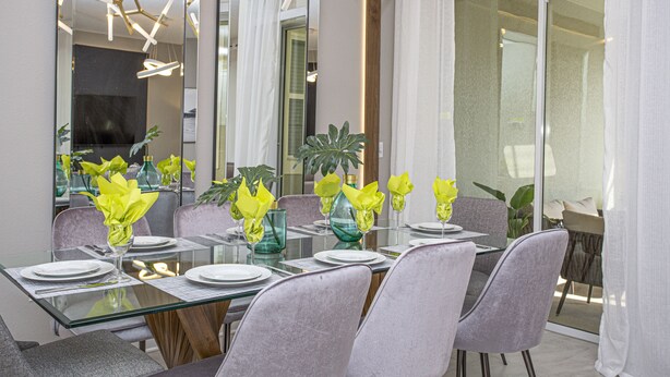 Un comedor moderno con una mesa de vidrio, sillas tapizadas en gris y servilletas amarillas.