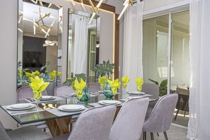 Een moderne eetruimte met een glazen tafel, grijs gestoffeerde stoelen en gele servetten.