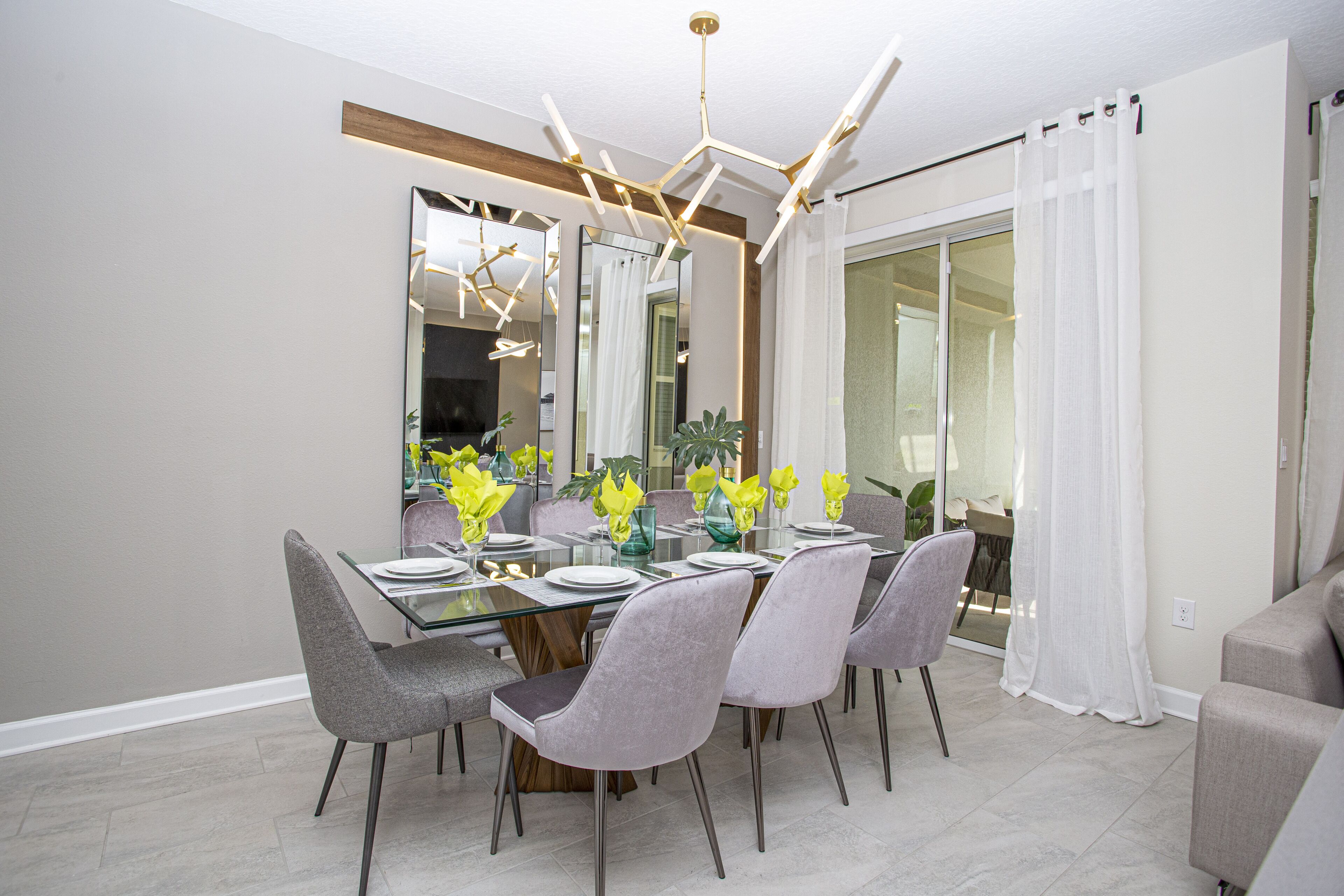 A dining area with a glass table, grey upholstered chairs, and a modern chandelier.