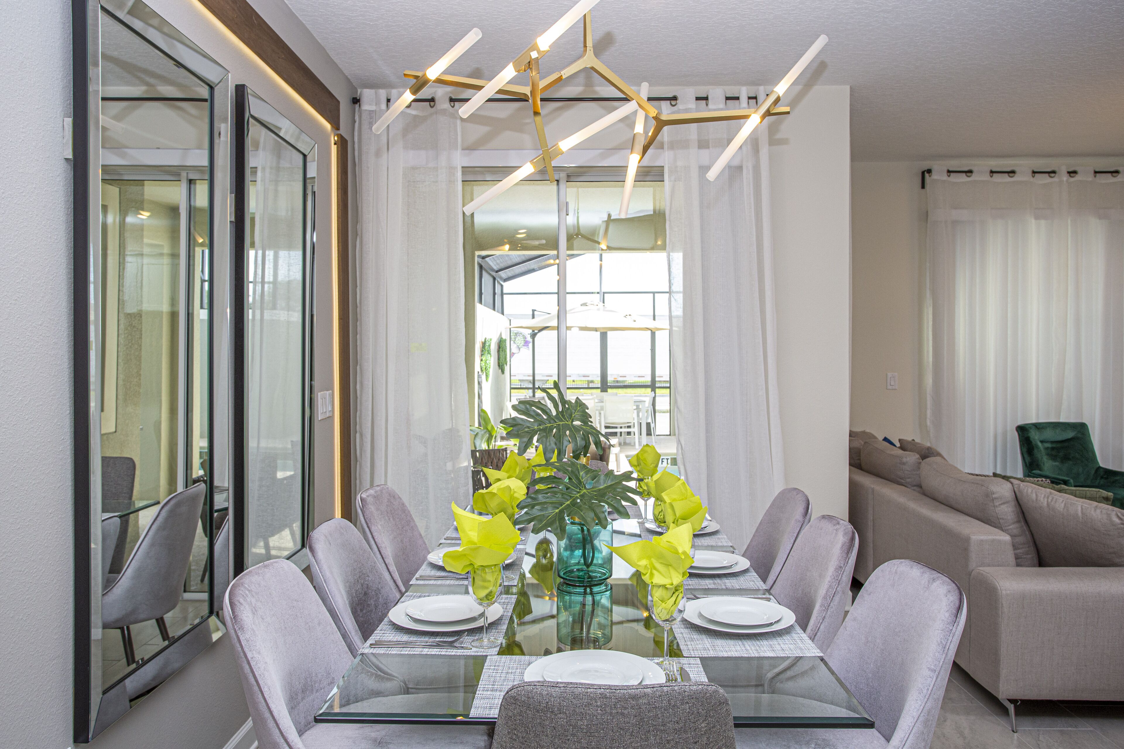 Un espace repas moderne avec une table en verre, des chaises à revêtement gris et une plante placée au centre.