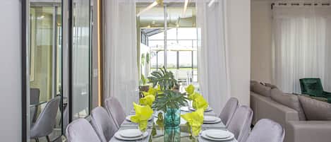 Un espace repas moderne avec une table en verre, des chaises à revêtement gris et une plante placée au centre.