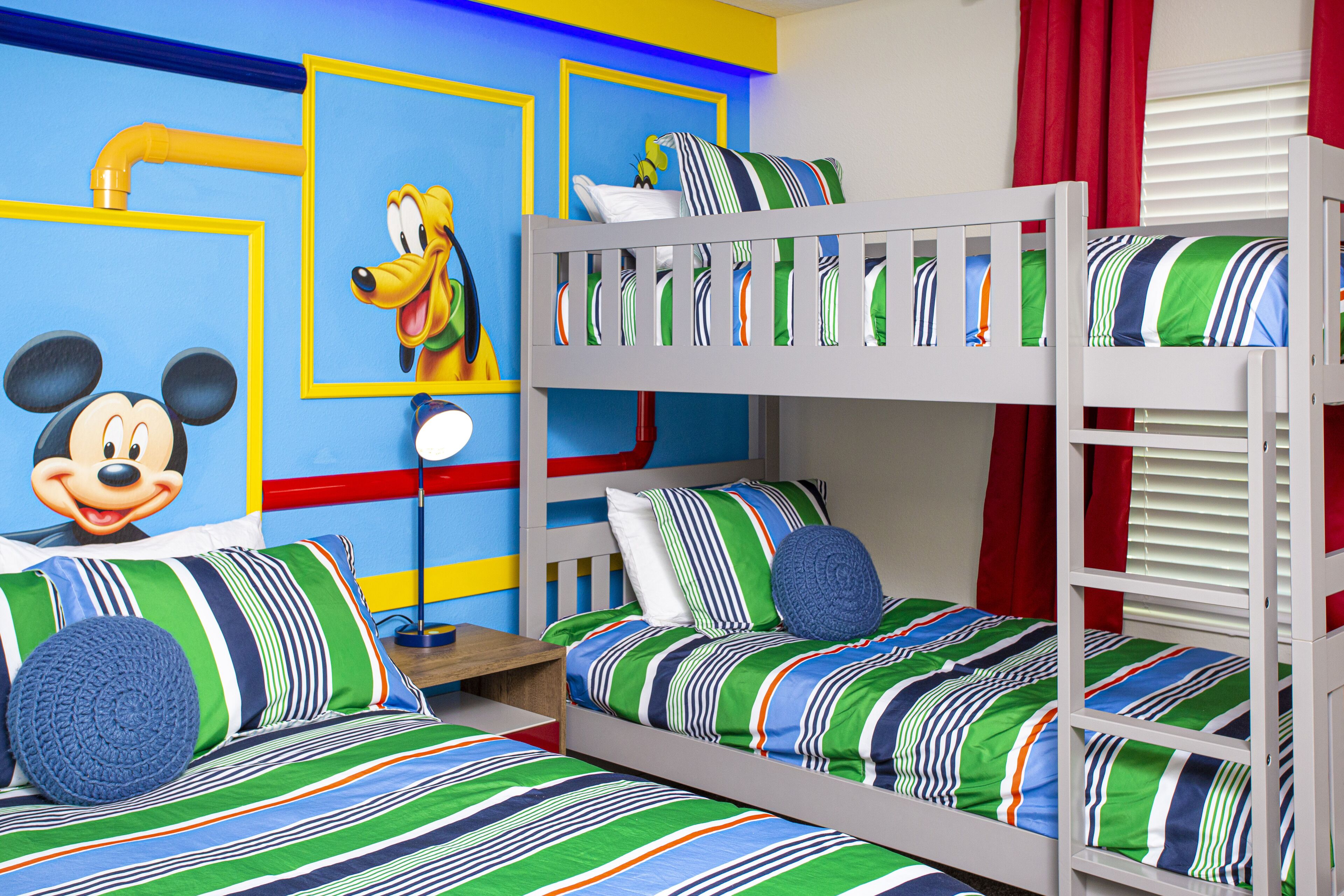 A children's room with bunk beds, Mickey Mouse wall art, and colorful striped bedding.