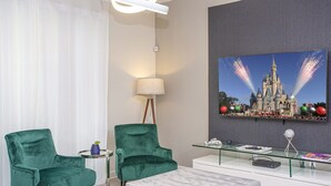 Una sala de estar moderna con dos sillones tapizados en terciopelo verde, una mesa de centro de vidrio, un sofá blanco y un cuadro grande con la imagen de un castillo.